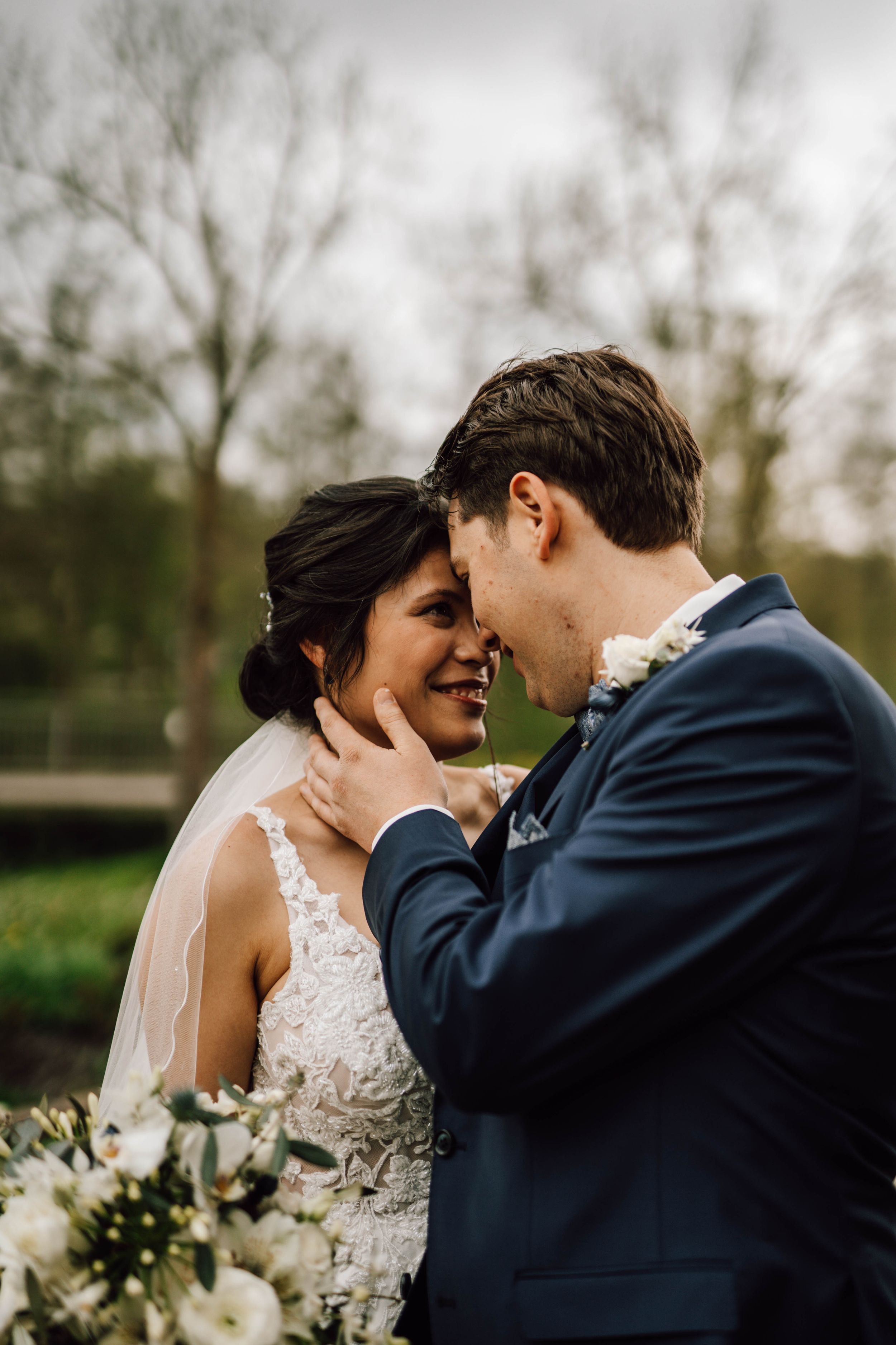A tender moment between newlyweds as they embrace outdoors with a white floral bouquet.
