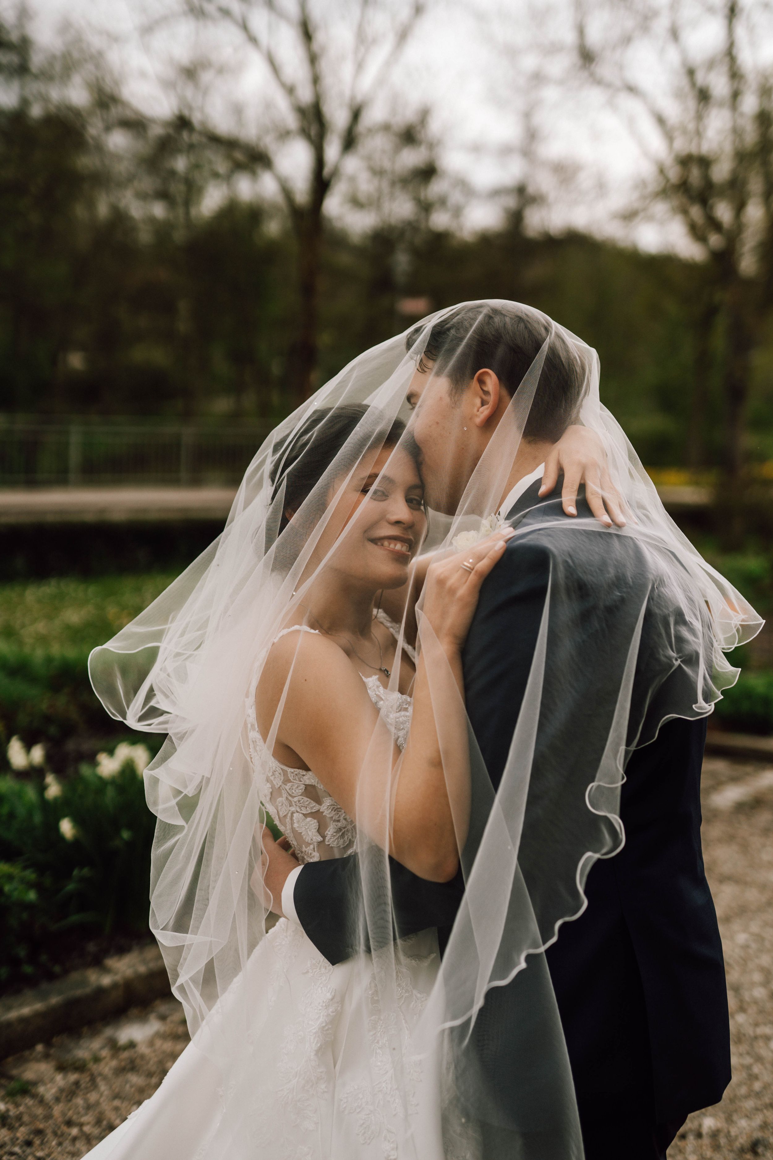 A romantic moment under a flowing veil as the newlyweds embrace in a garden setting.