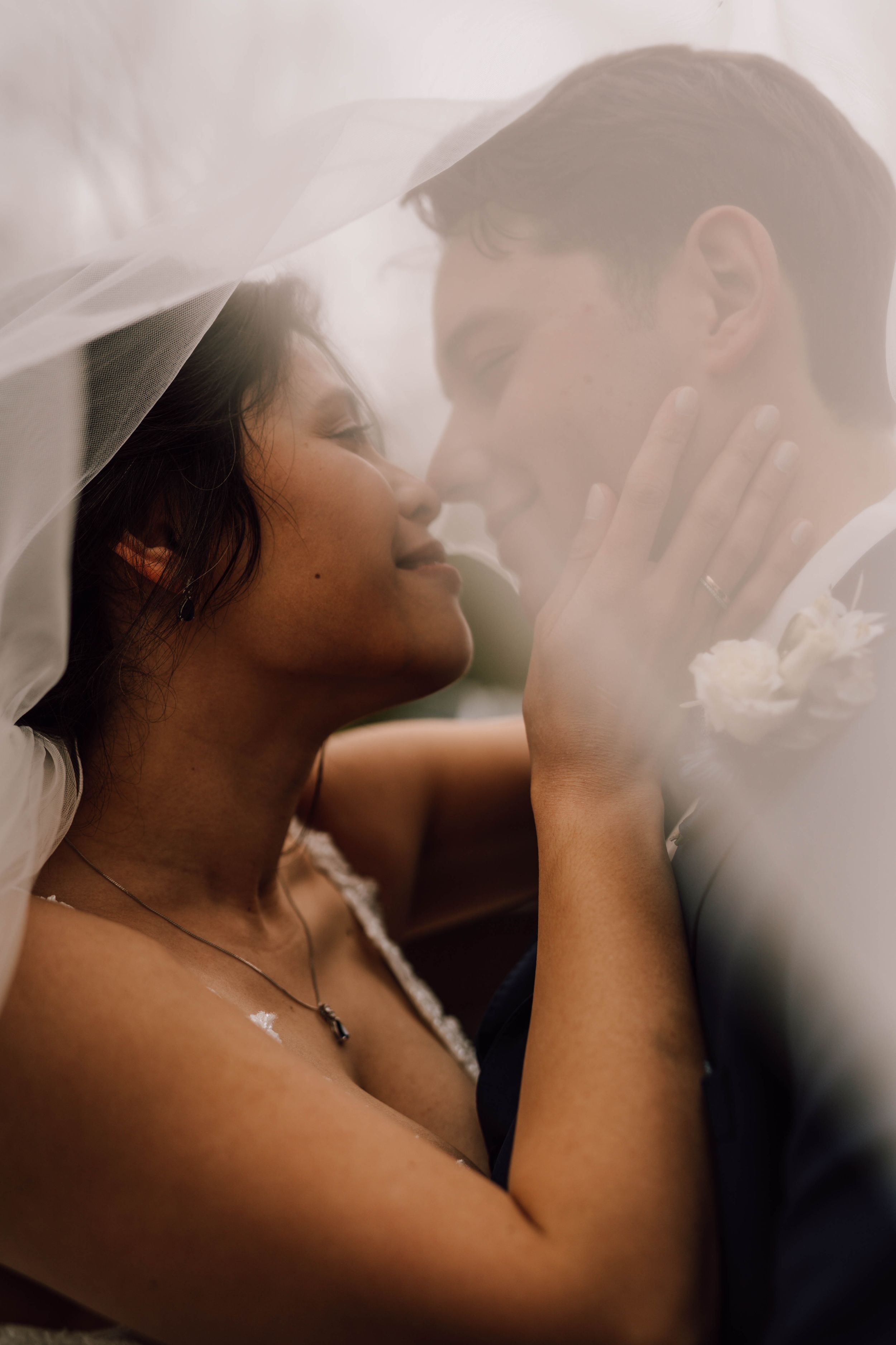 An intimate moment captured under a sheer veil as newlyweds share a tender embrace.