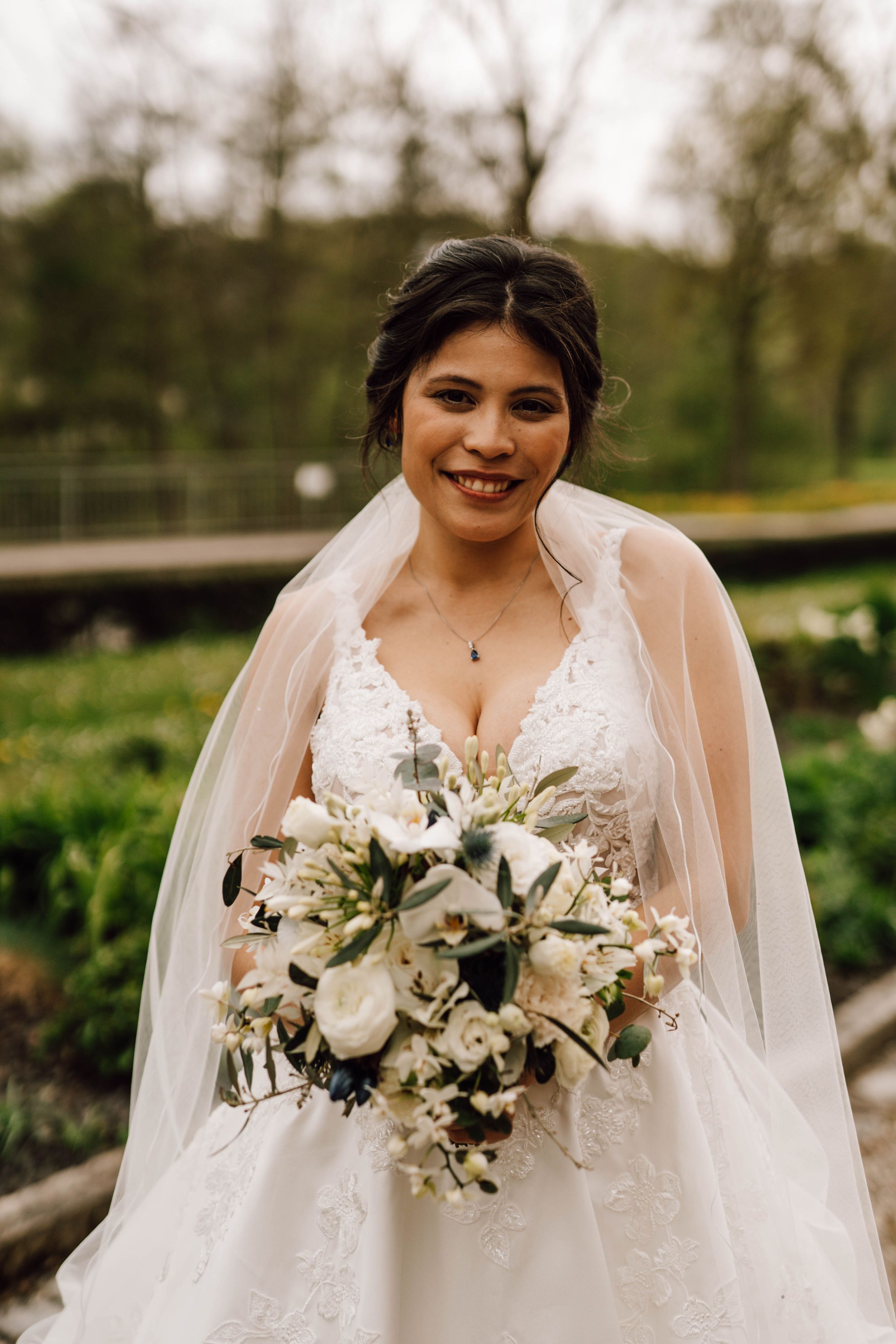 Elegant white bridal bouquet featuring white roses and greenery against an outdoor garden backdrop.