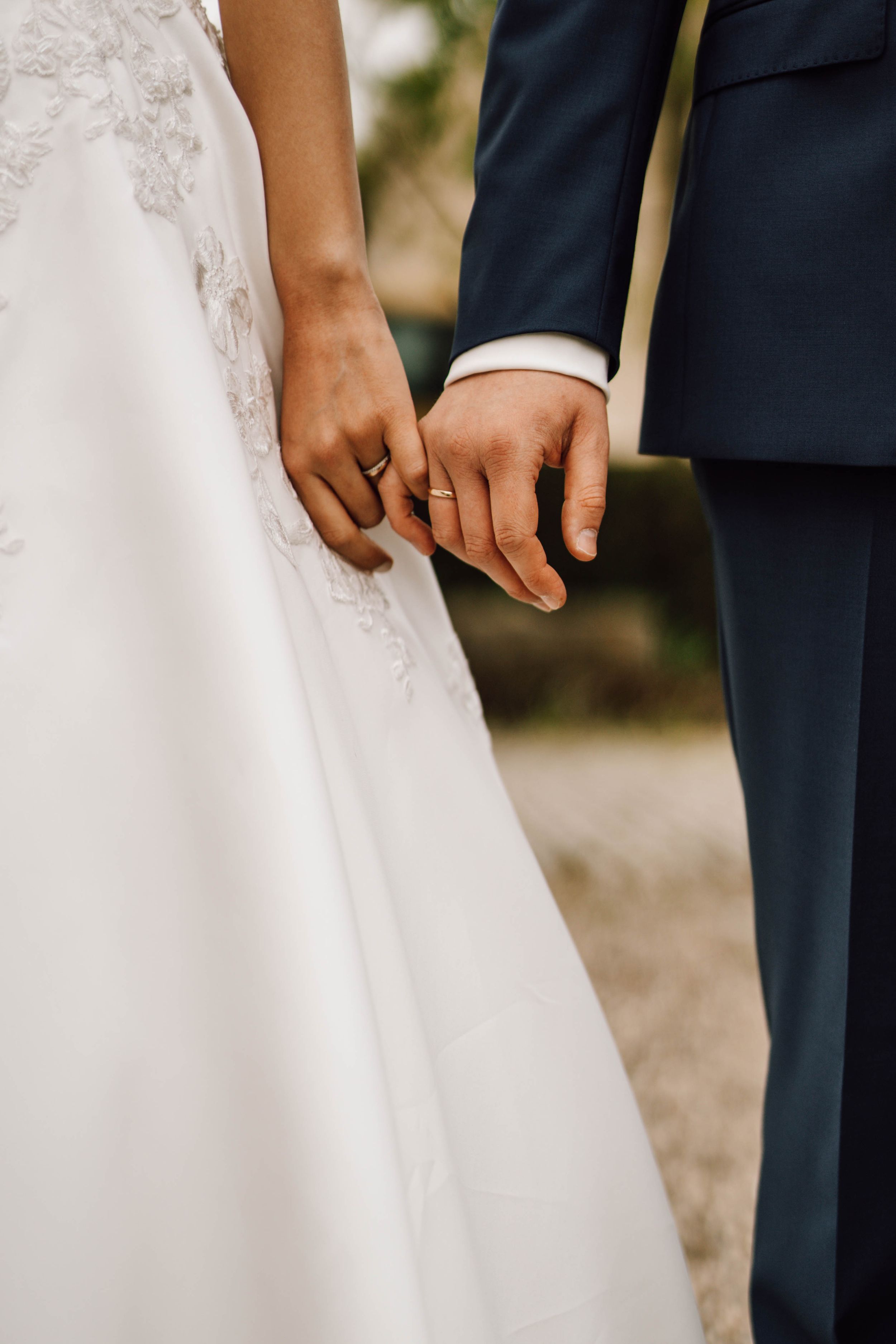 Close-up of hands and wedding attire showing white lace dress and navy suit details.