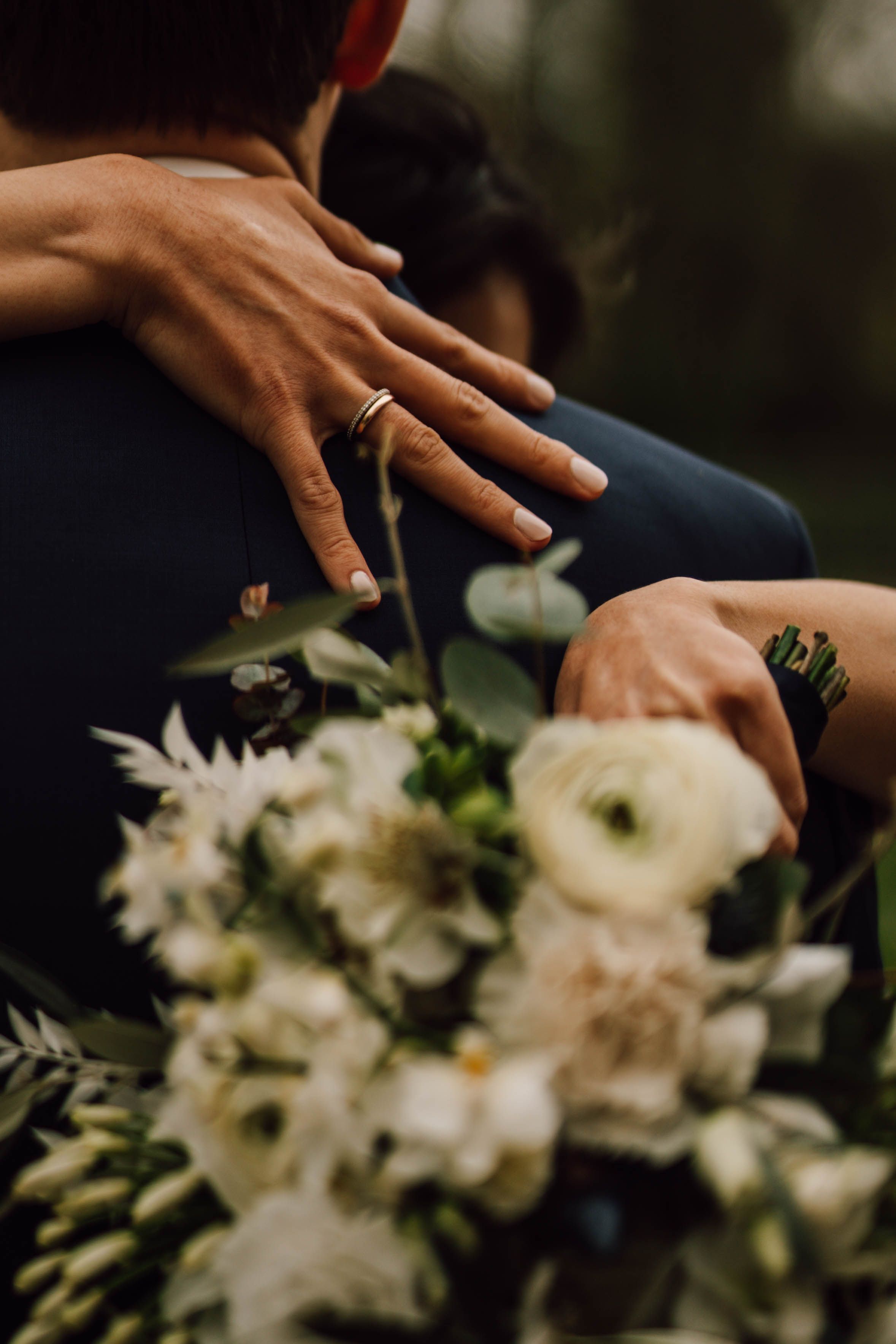 Close-up of hands resting on white wedding bouquet with delicate flowers.
