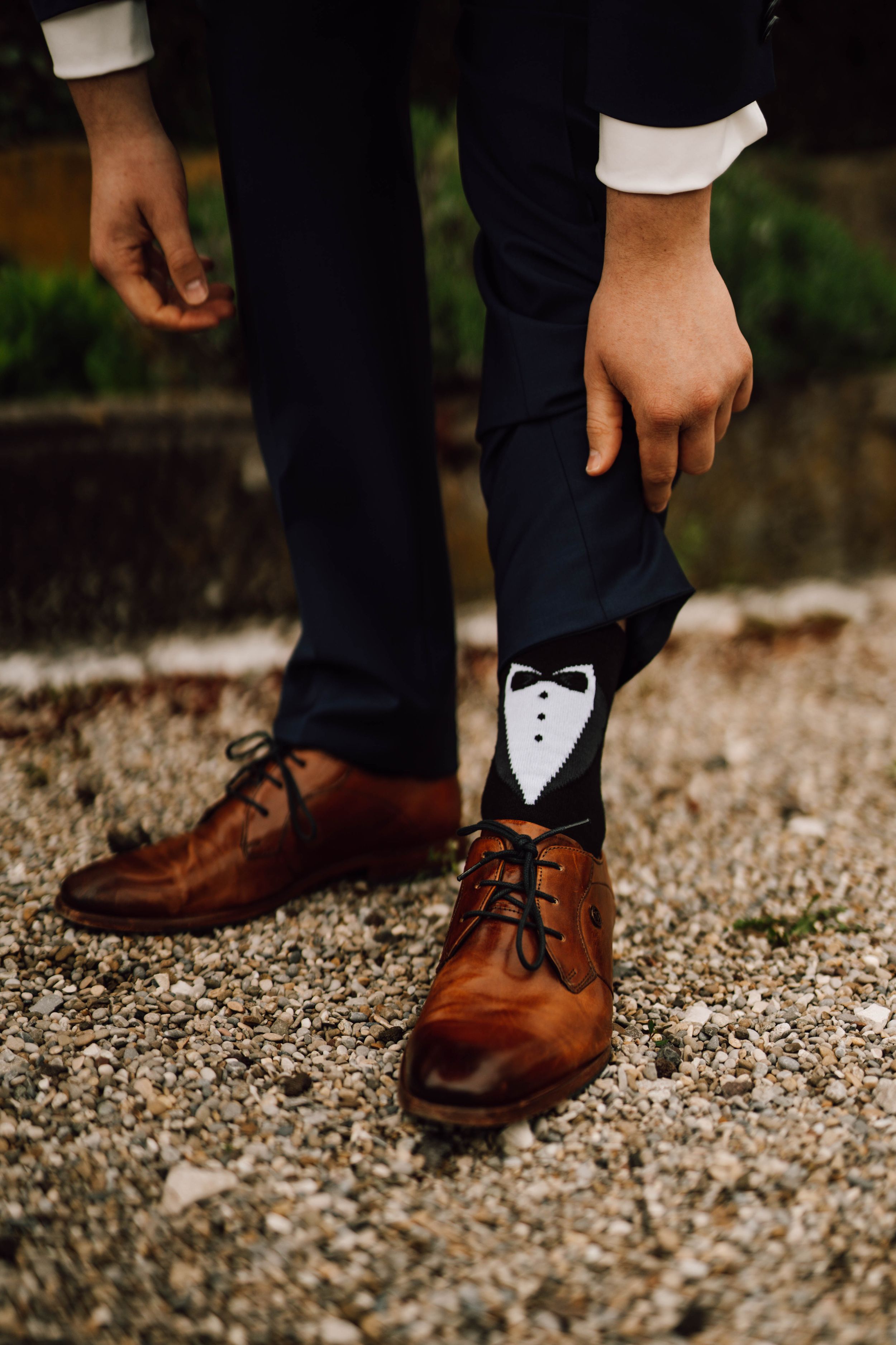 Brown leather dress shoes on gravel ground worn with navy suit pants.