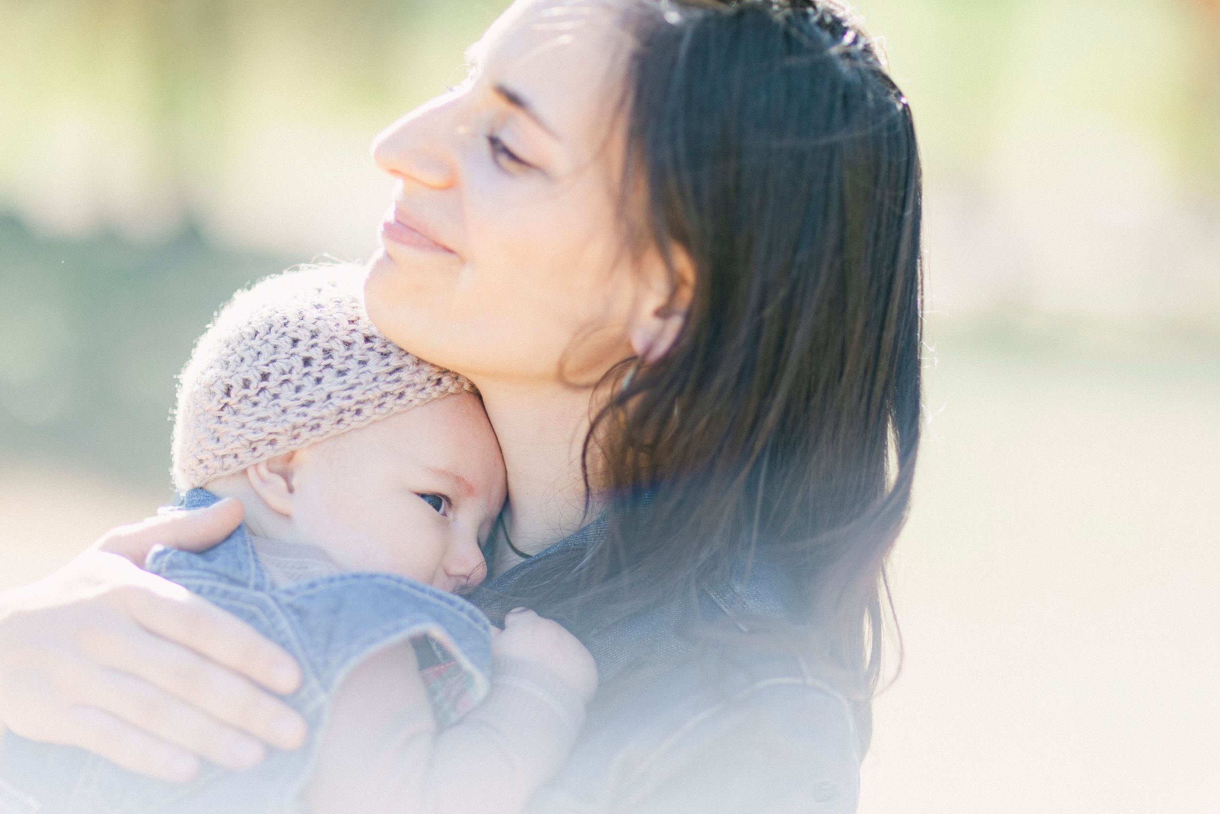 Tender moment between parent and baby in soft dreamy lighting outdoors.