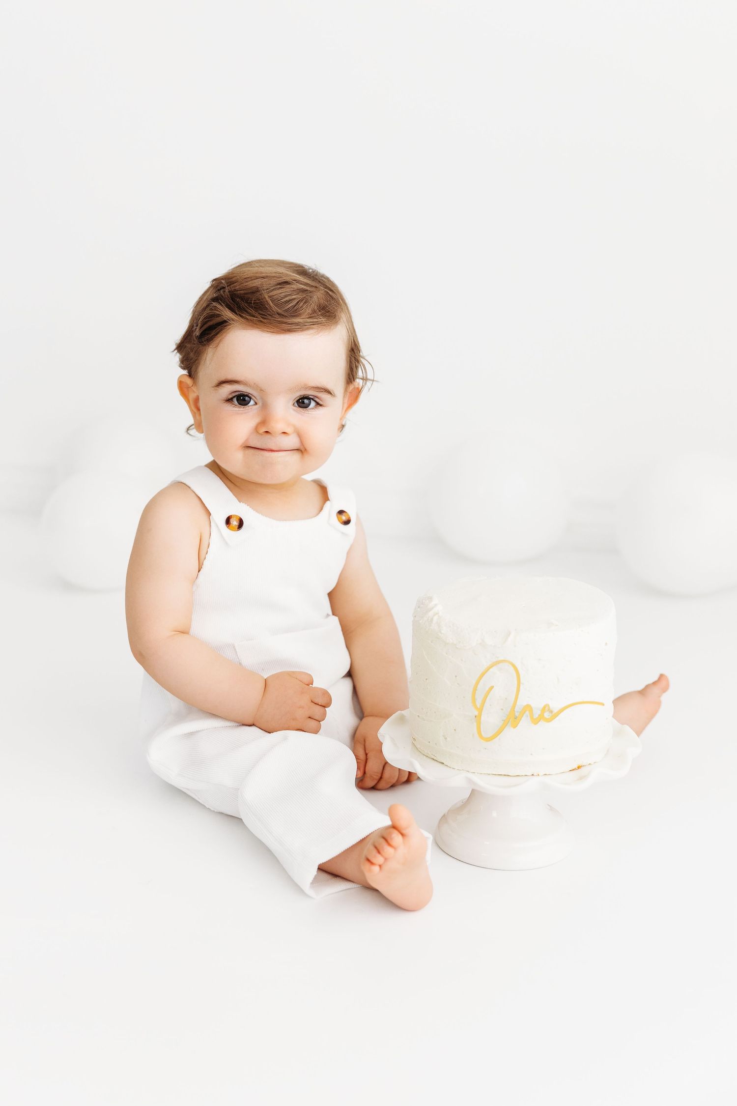 Adorable, happy one year old with a white cake and white balloons