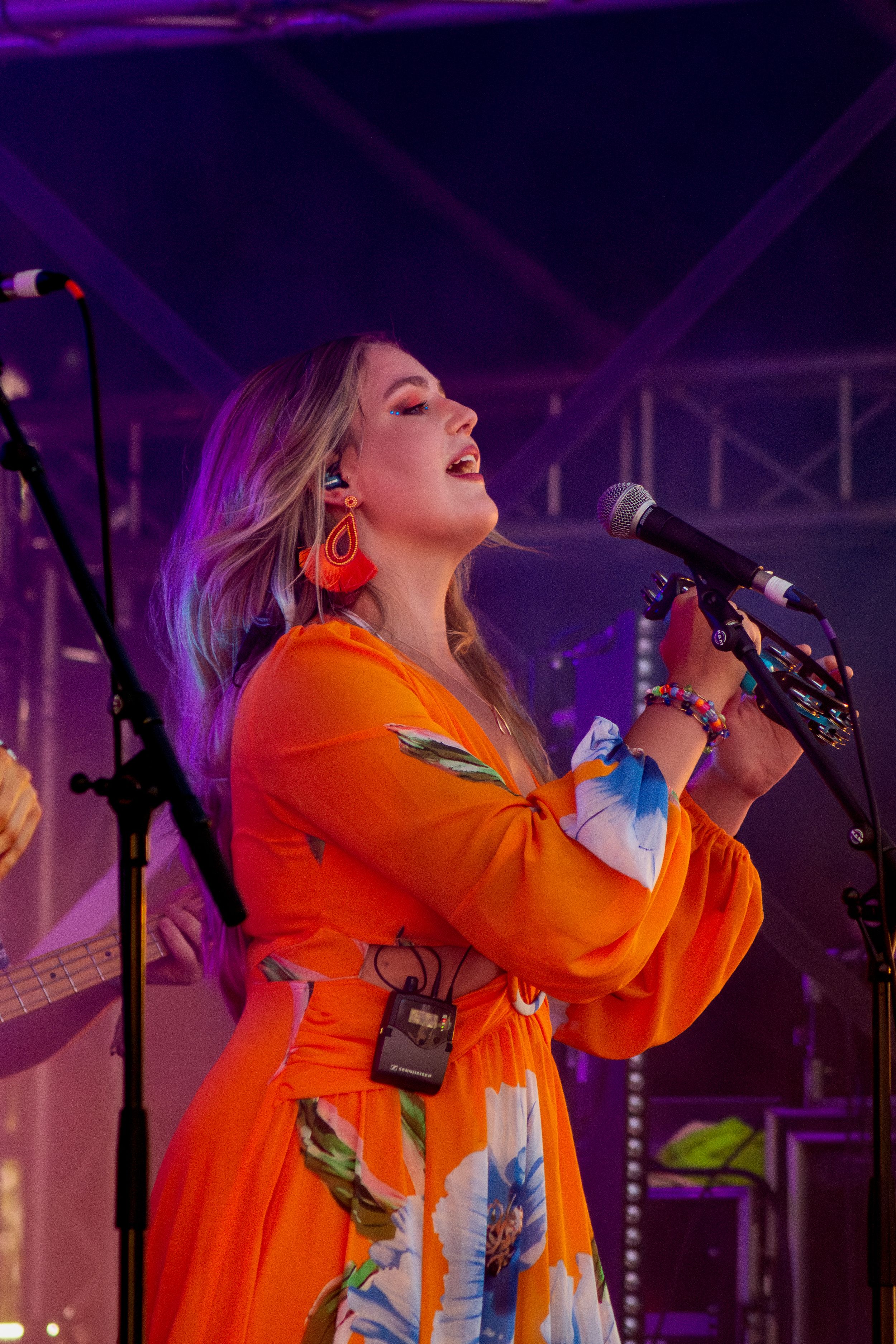 Singer in vibrant orange dress performing passionately on stage under purple lights.