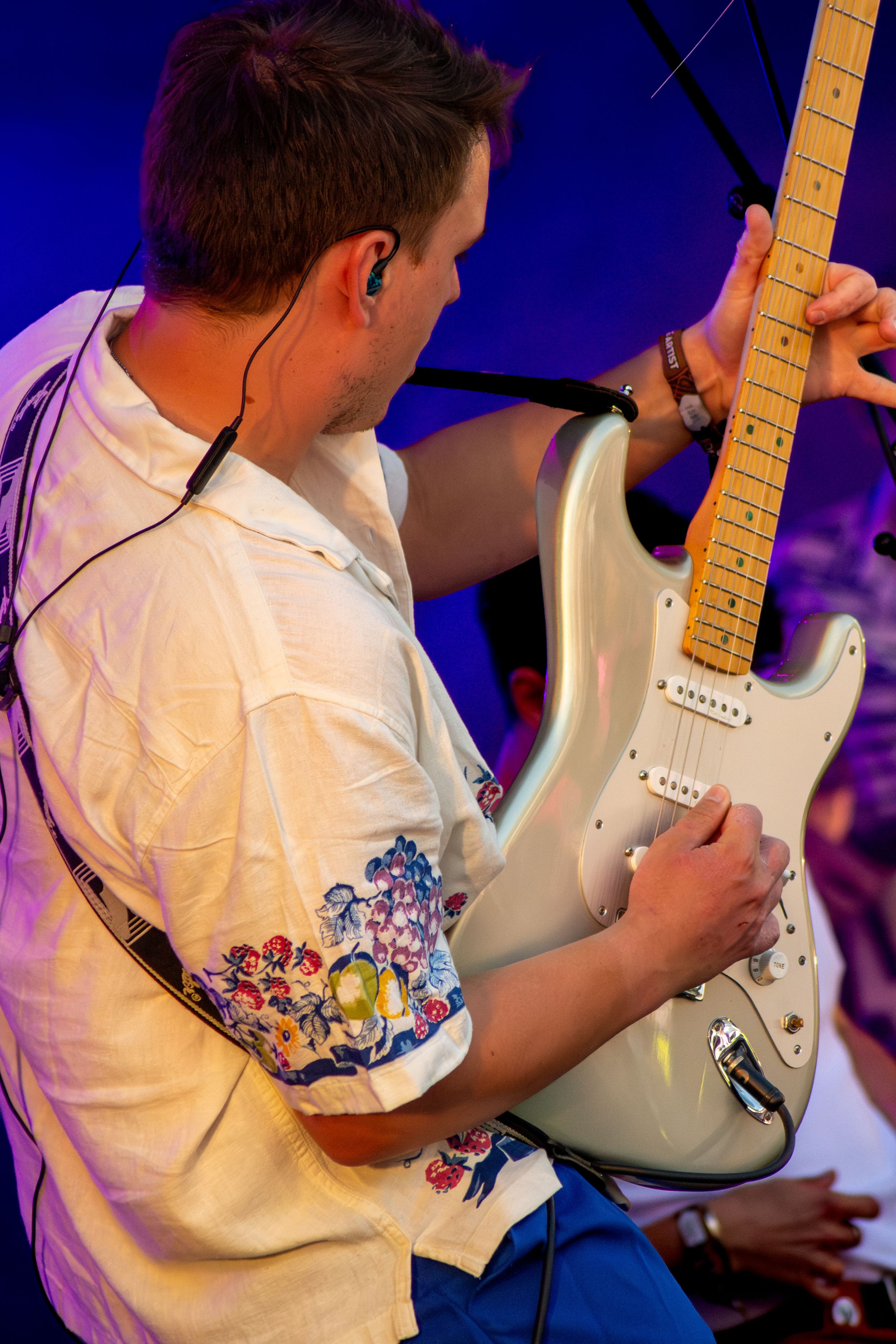 Musician playing silver Fender Stratocaster guitar under blue stage lighting.