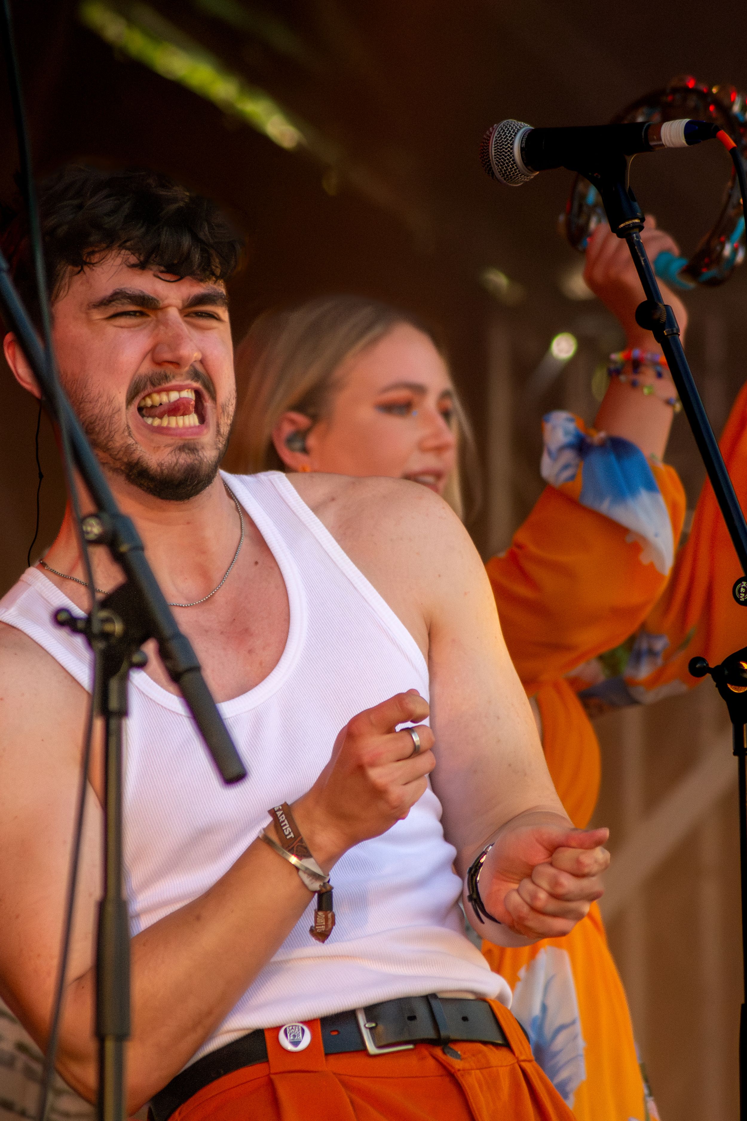 Energetic performer in white tank top singing passionately on stage with microphone.