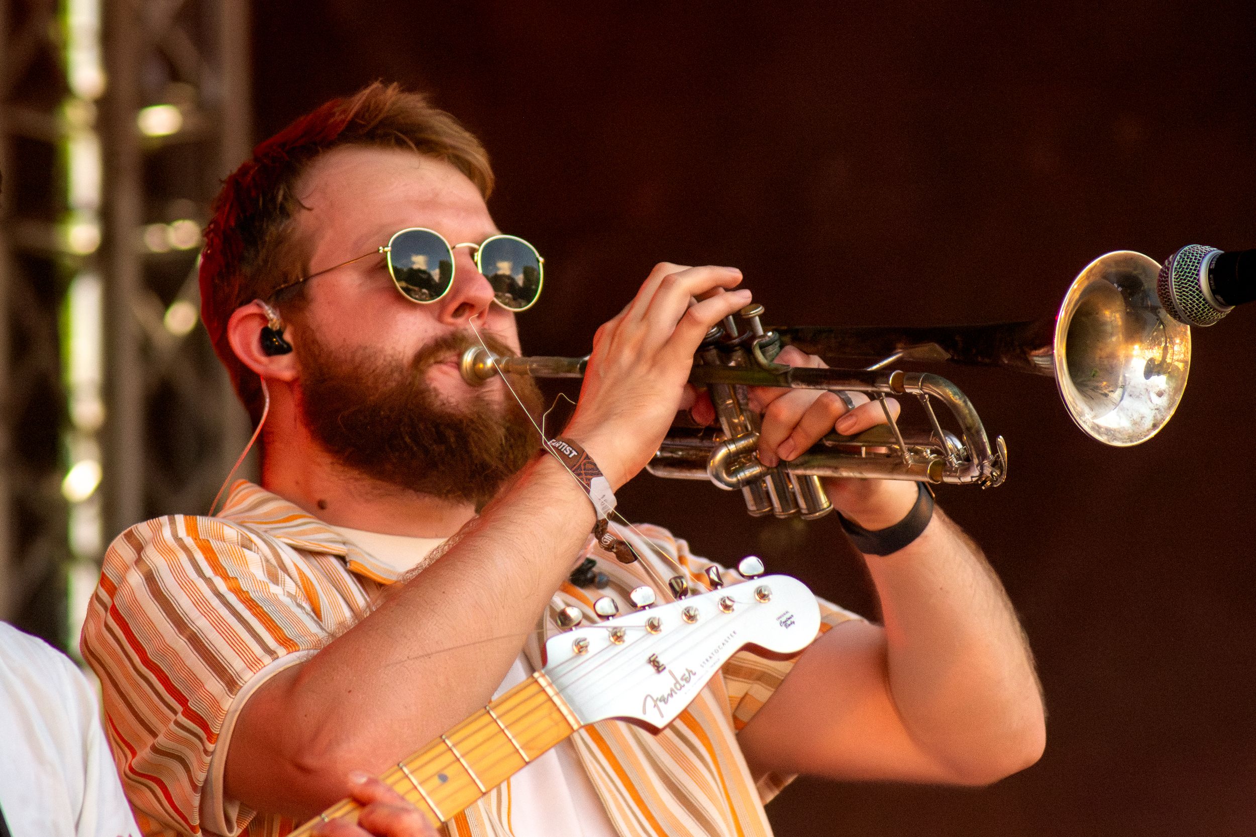 Close-up of trumpet player wearing sunglasses and striped shirt during performance.