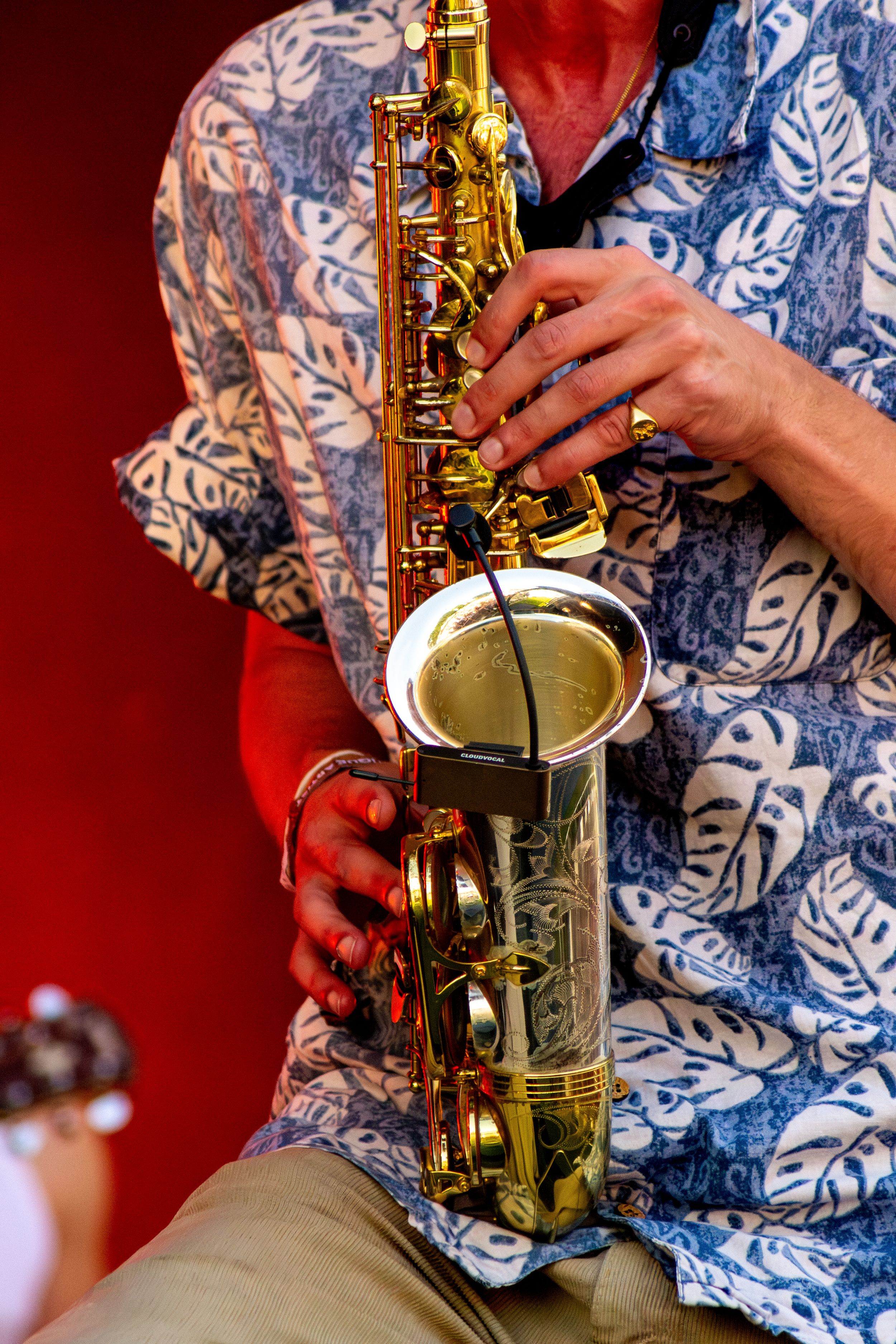 Close-up shot of hands playing saxophone in blue and white patterned shirt.