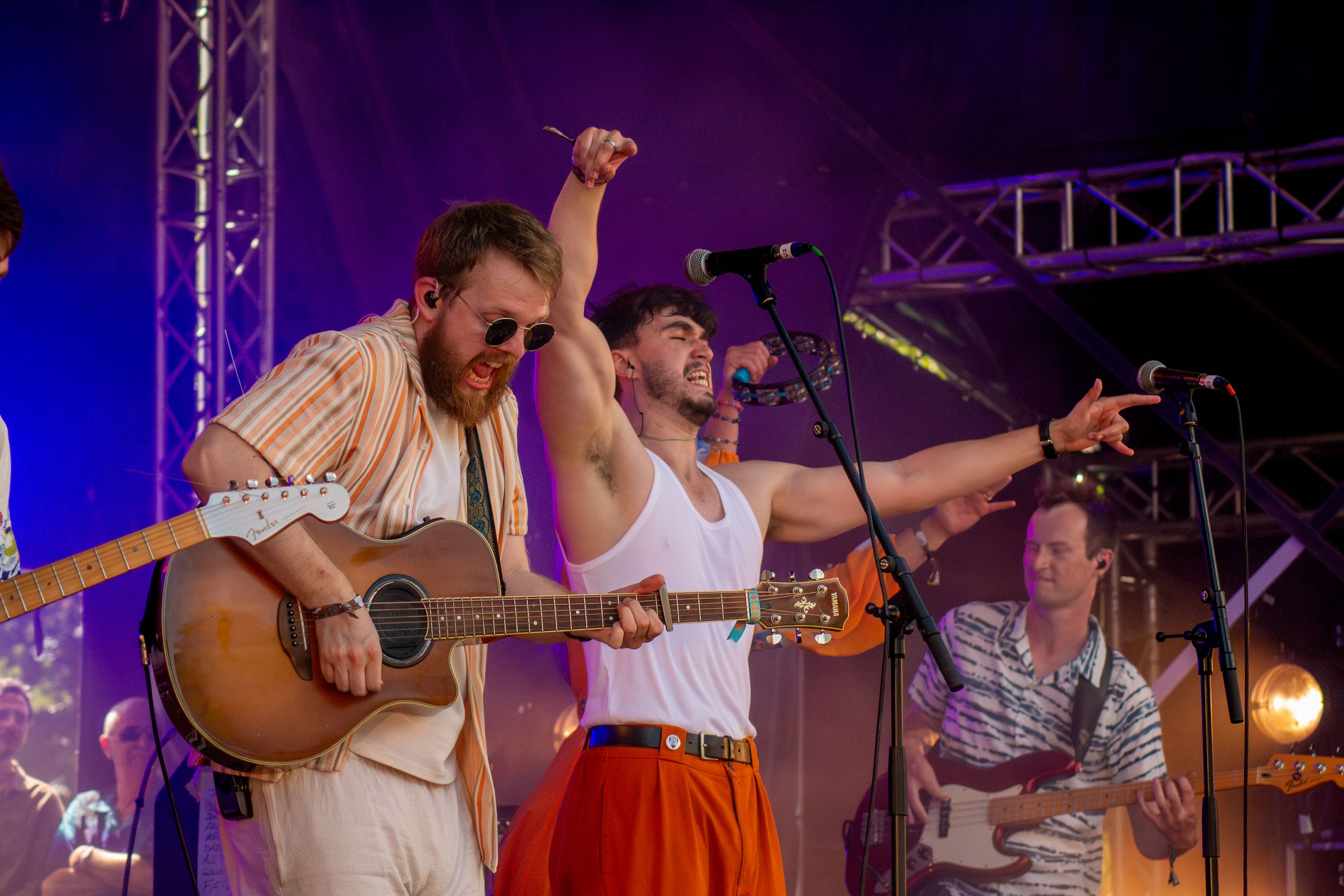 Band members performing together on outdoor stage with guitar and microphones.