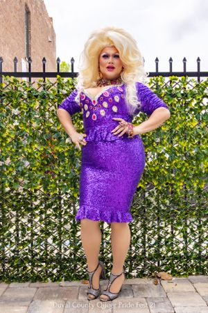 Performer in sparkly purple dress poses against ivy-covered fence backdrop.