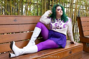 Person in purple outfit relaxes on wooden bench against bamboo backdrop.
