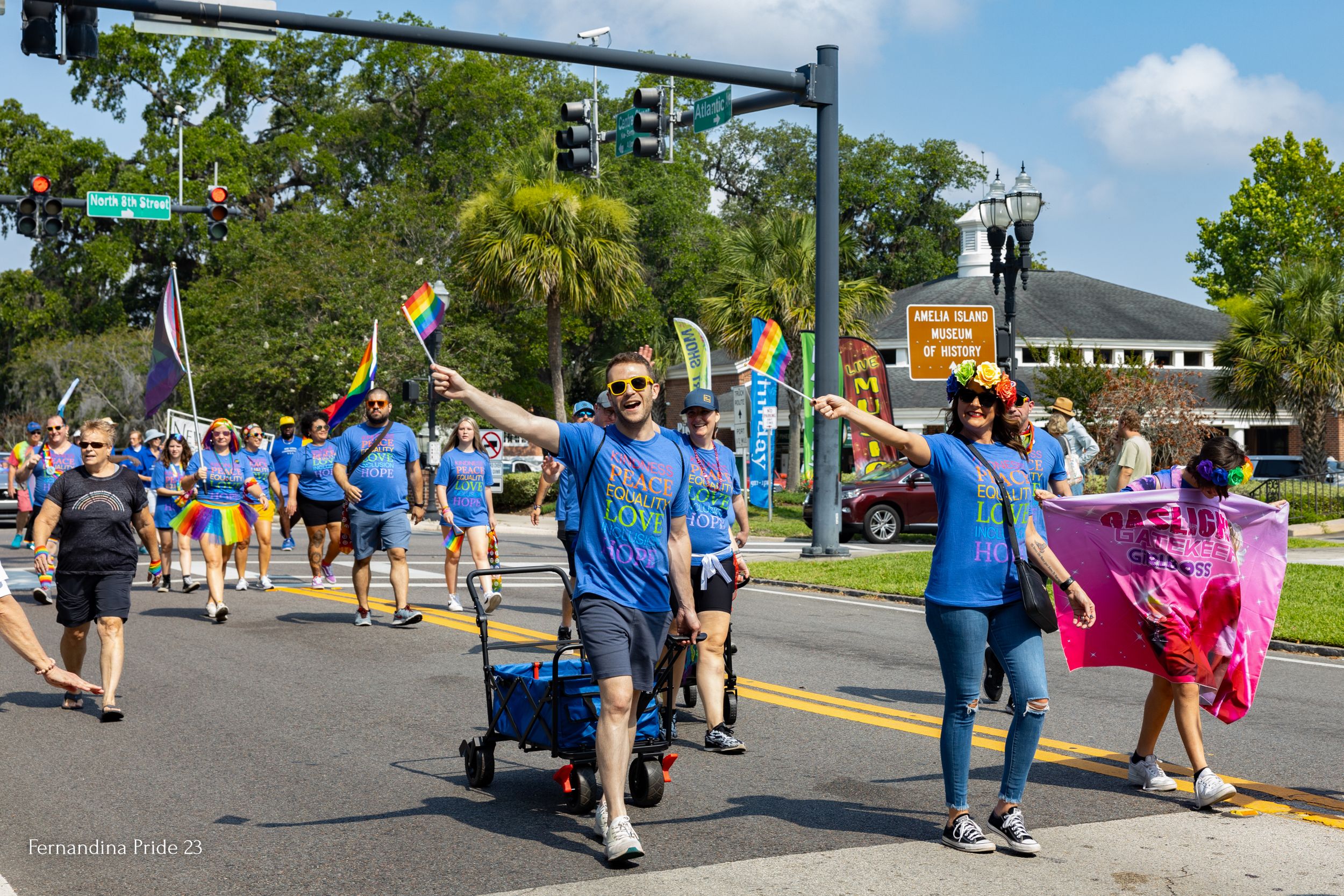 Festival participants walking down sunny street with strollers and colorful decorations.