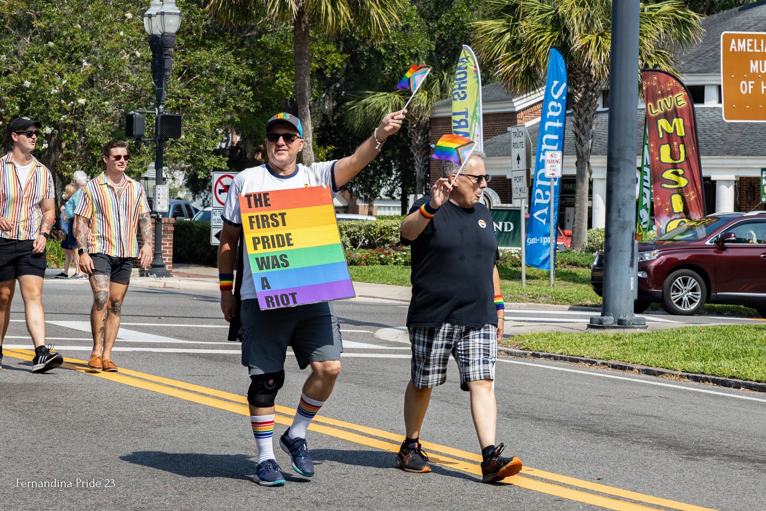 Participants walking in a pride parade carrying a rainbow flag on a city street.