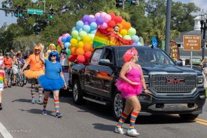 Colorful pride parade float featuring a GMC truck decorated with rainbow balloons on a sunny day.