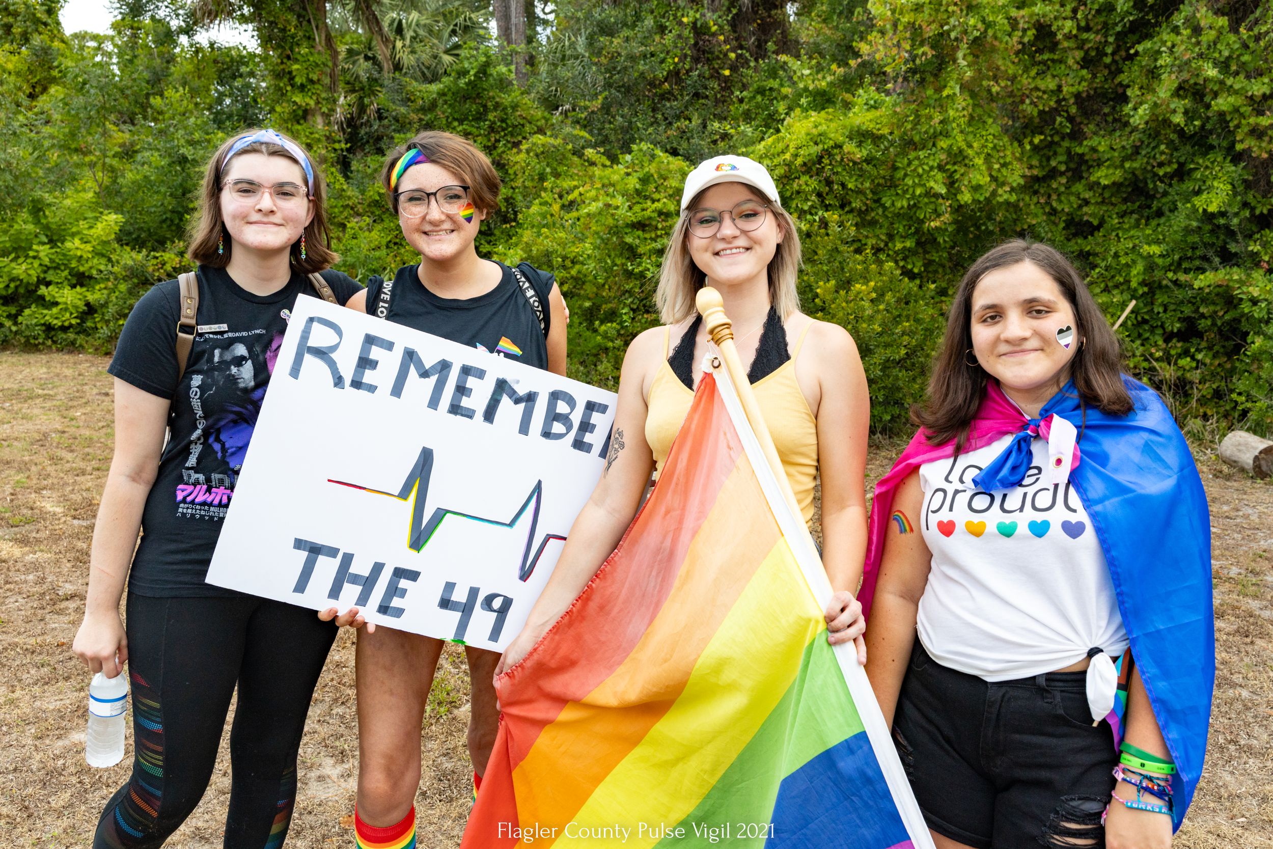 Attendees at a pride event show support with colorful flags and signs in an outdoor setting.