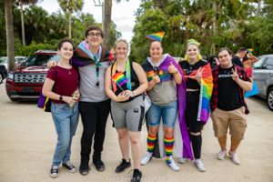 Group celebrates at pride event with rainbow flags and accessories outdoors.