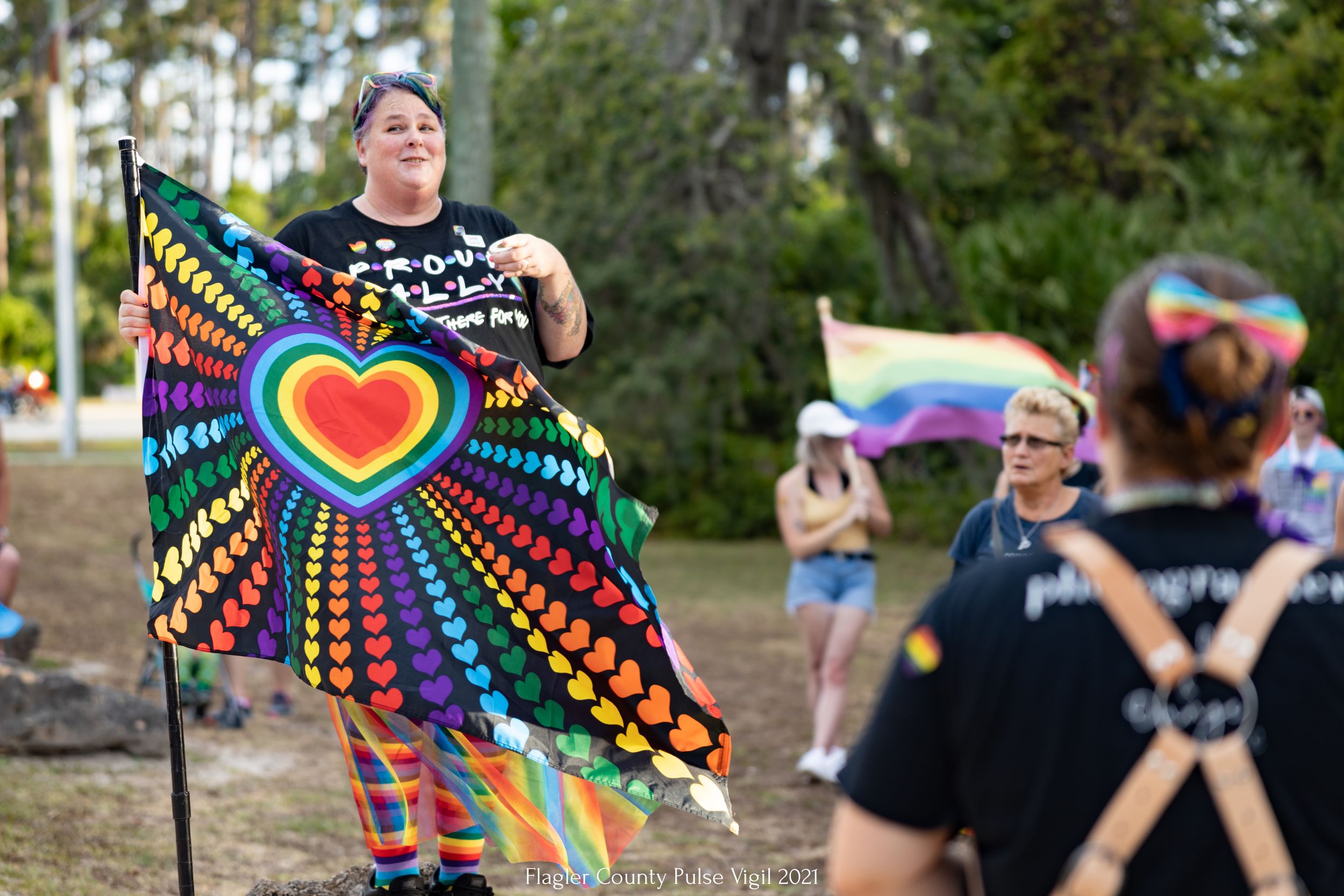 Person displays vibrant rainbow heart flag at outdoor pride celebration.