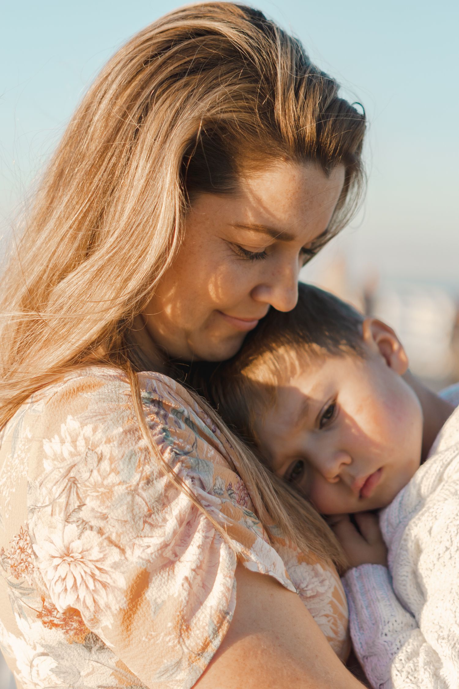 A mother tenderly holds her young child close in warm golden sunlight in an emotional portrait.