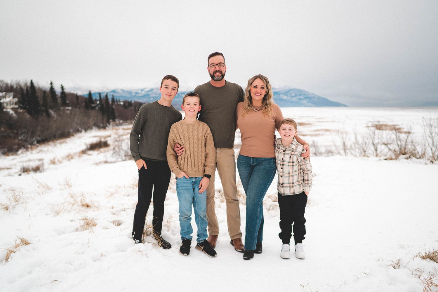 Family of five posing together in snowy winter landscape with mountains in background.