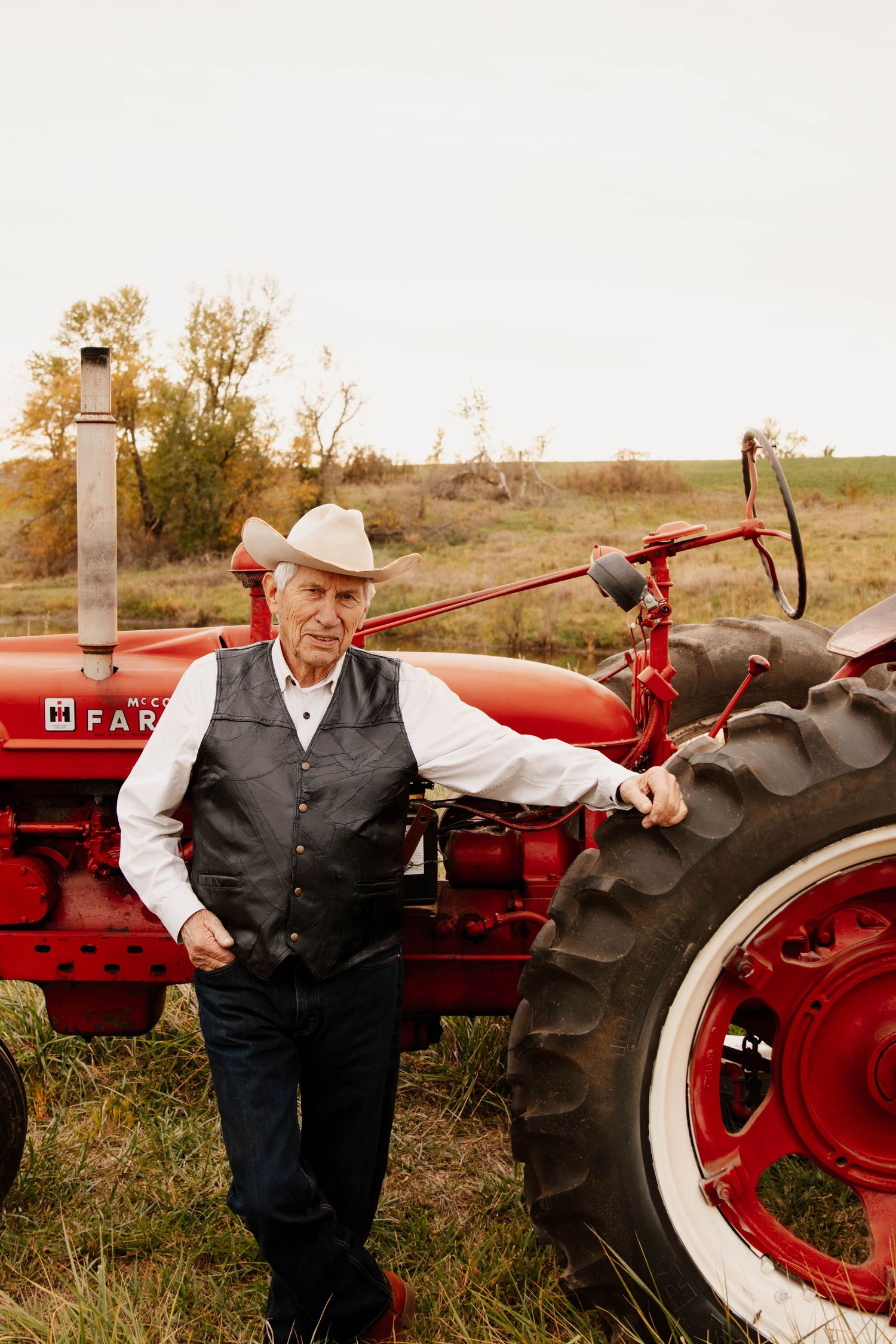 A classic red Farmall tractor stands out against a rural landscape while someone poses beside it.