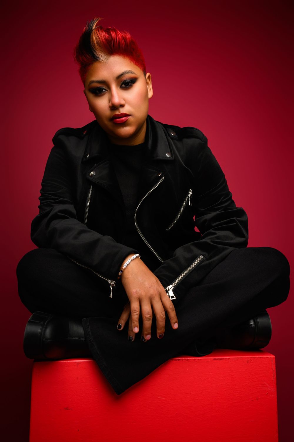 Dancer model in black leather jacket poses dramatically against red backdrop in professional portrait series.