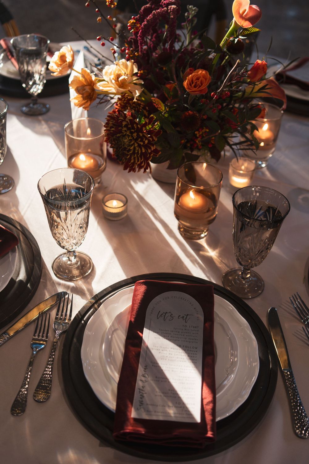 Elegant wedding table setting with black charger plates, crystal glasses, and moody floral centerpieces lit by candlelight.