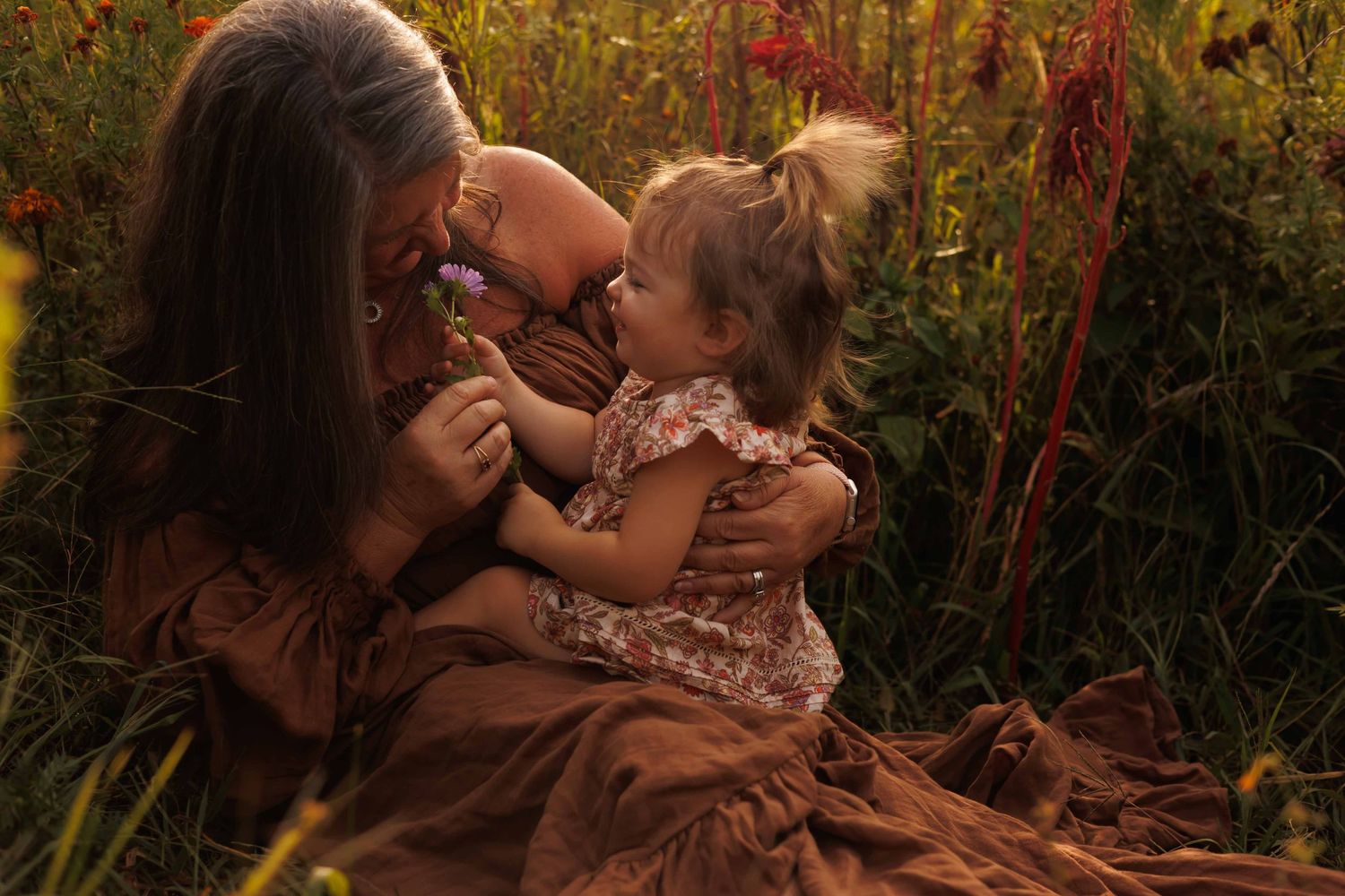 Parent and child embracing in a field of red wildflowers during sunset.