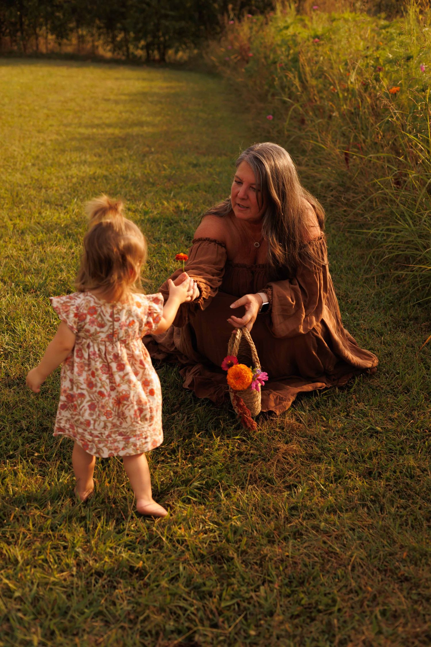 Two people play in a field during sunset with orange flowers and tall grass.