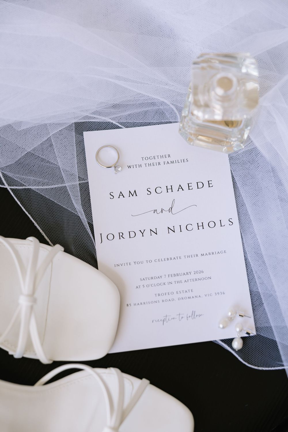 Elegant wedding flat lay featuring Sam Schaede and Jordyn Nichols invitation, bridal heels, veil, ring, and perfume.