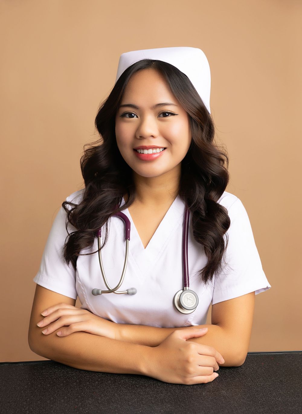Medical professional wearing white uniform and cap with stethoscope poses against warm background.