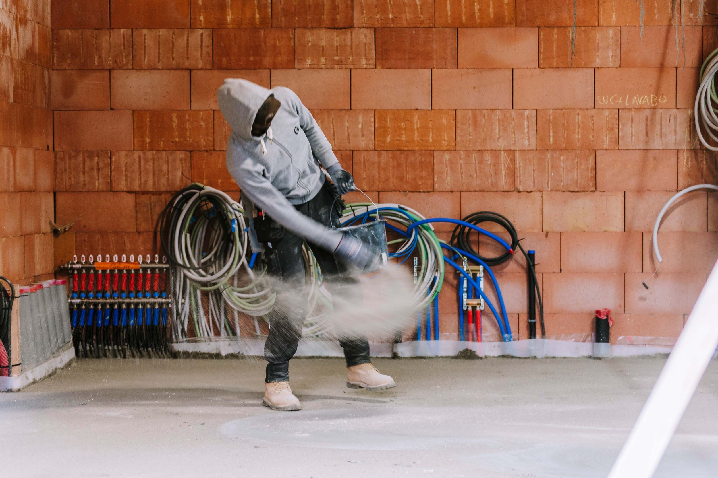 A person performs a skateboarding trick on a ramp against a red brick wall background.