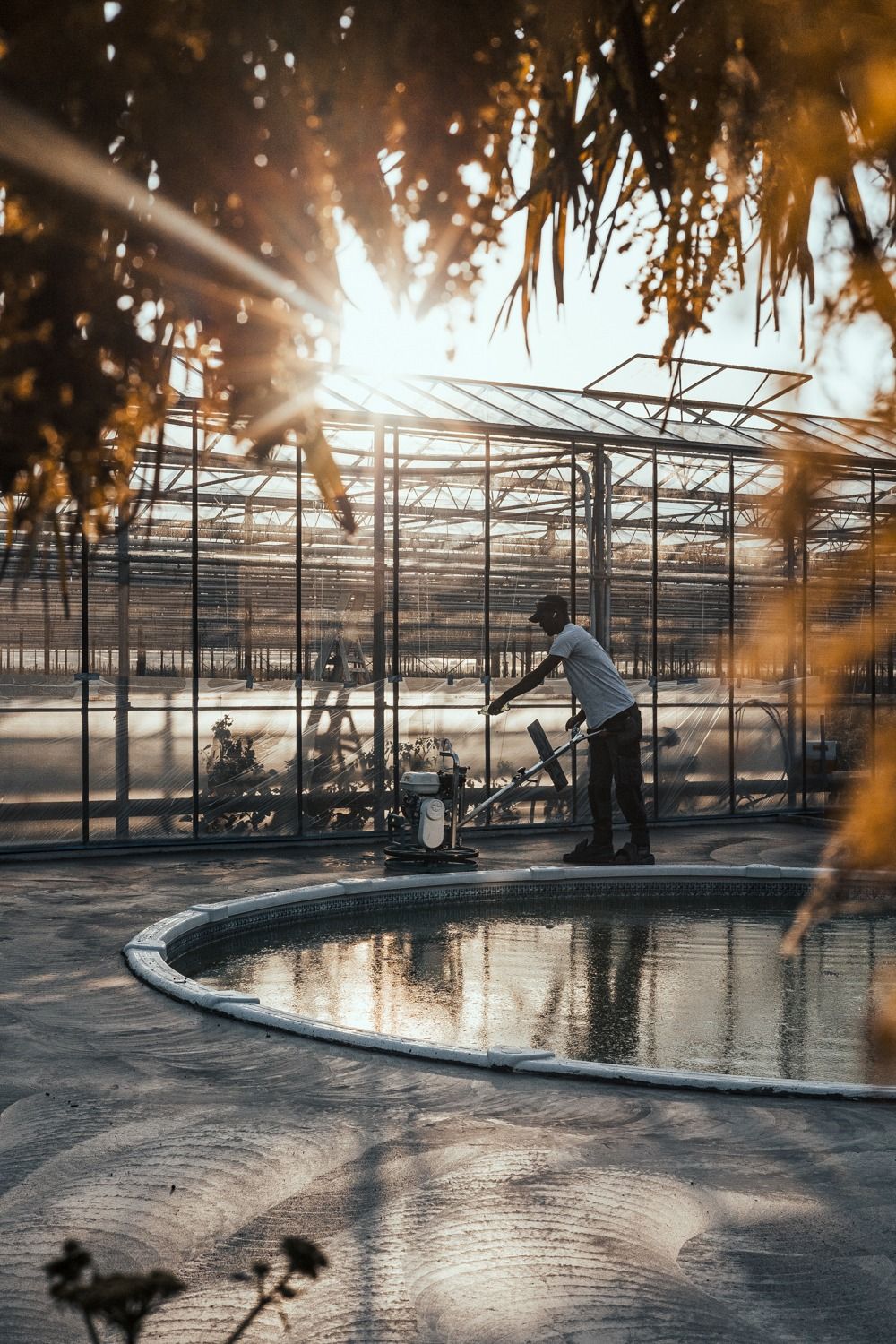 A serene indoor pool at sunset with sunlight streaming through glass windows creating dramatic reflections on the water.