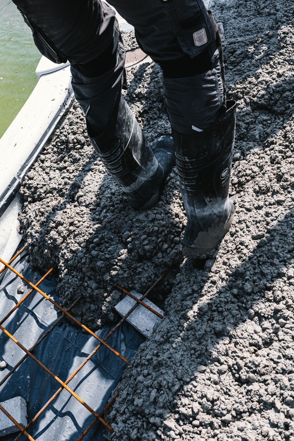 Person wearing black boots stepping through muddy terrain while installing metal grid walkway sections.