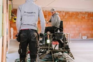 Workers in safety gear installing or repairing equipment in an industrial warehouse setting.