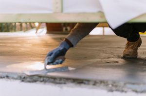 Worker applying concrete floor leveling compound with a trowel in a construction site.