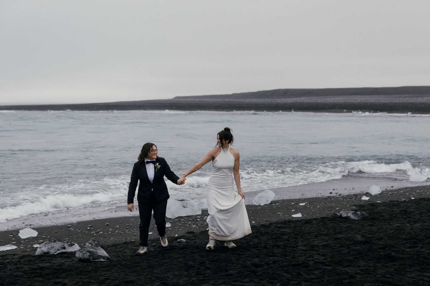 Two people dance playfully together on a misty beach with rocky cliffs in the background.