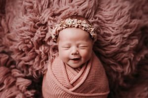 Perfect smiling baby at her newborn session cuddled on a pink fur rug