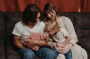 A family relaxes together on a dark leather couch, sharing an intimate moment with their sleeping newborn baby.