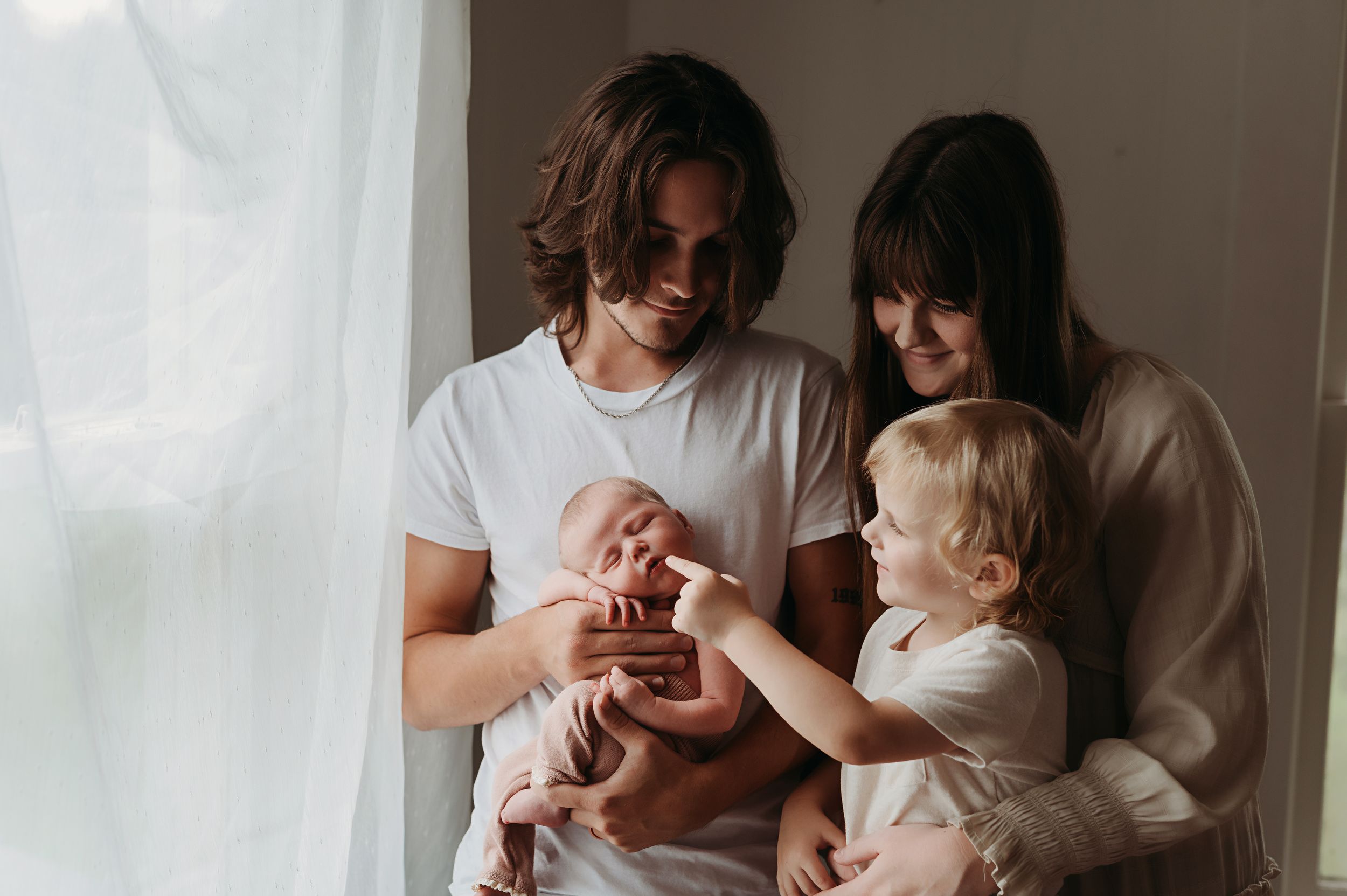 An in home newborn session with the family standing by the window.