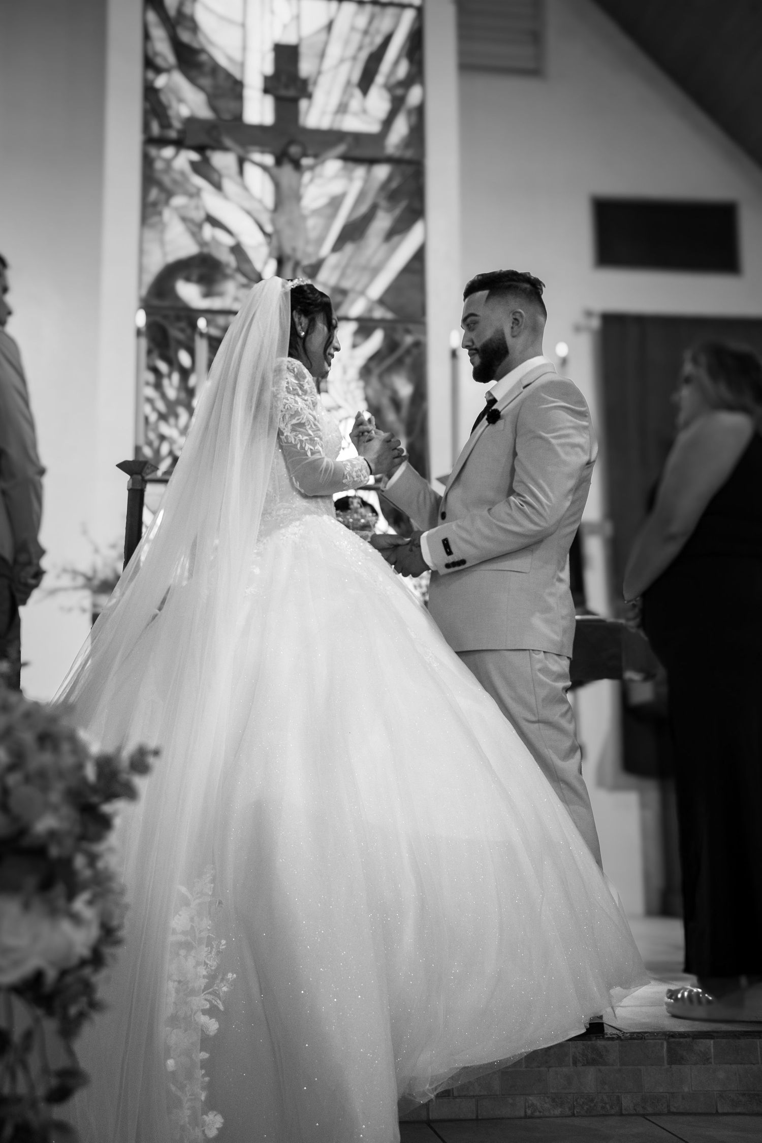 Black and white photo of a bride and groom exchanging vows at a church altar during their wedding ceremony.