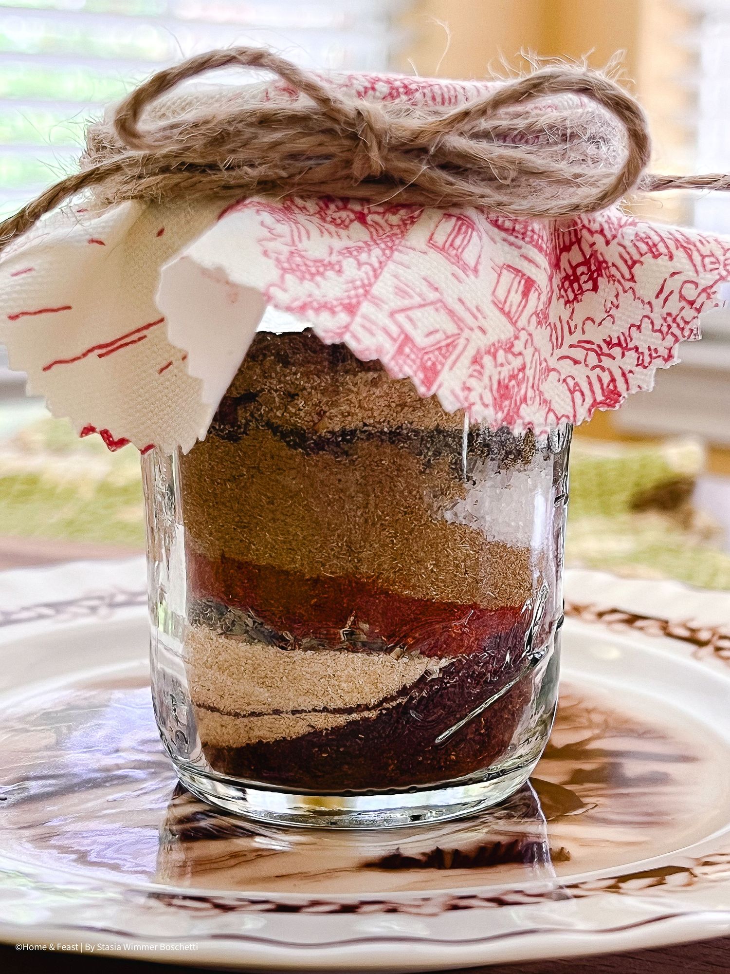 Multiple glass jars containing layers of dry chocolate cake ingredients with decorative cloth tops.