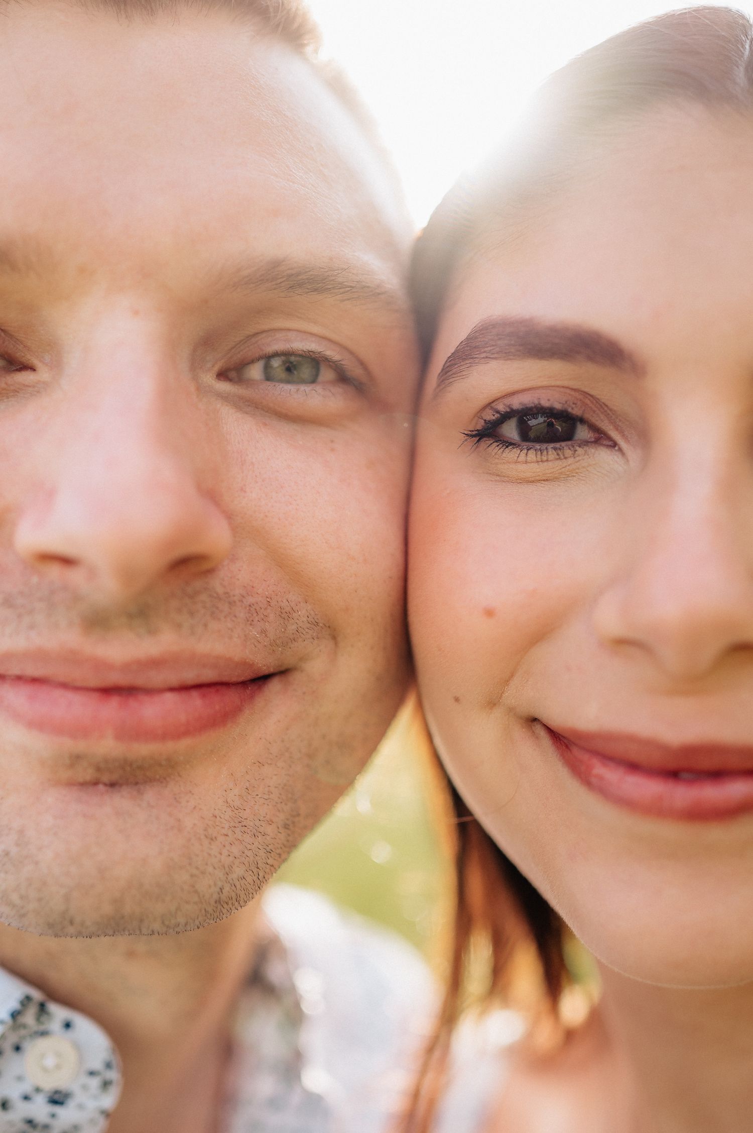 Close-up portrait of couple with warm smiles in sunlit outdoor setting.