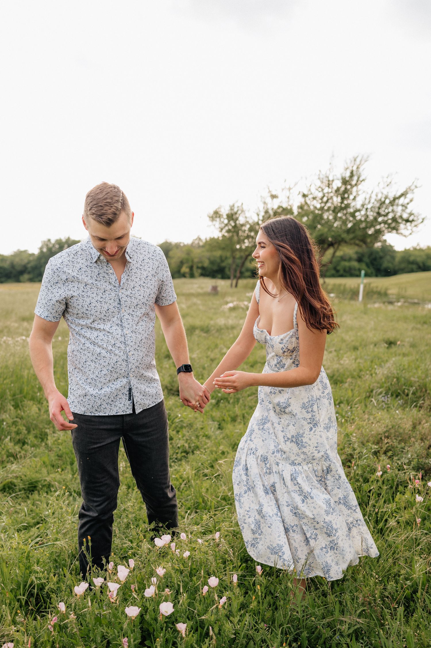 A couple holding hands and dancing in a summer field wearing floral and patterned outfits.