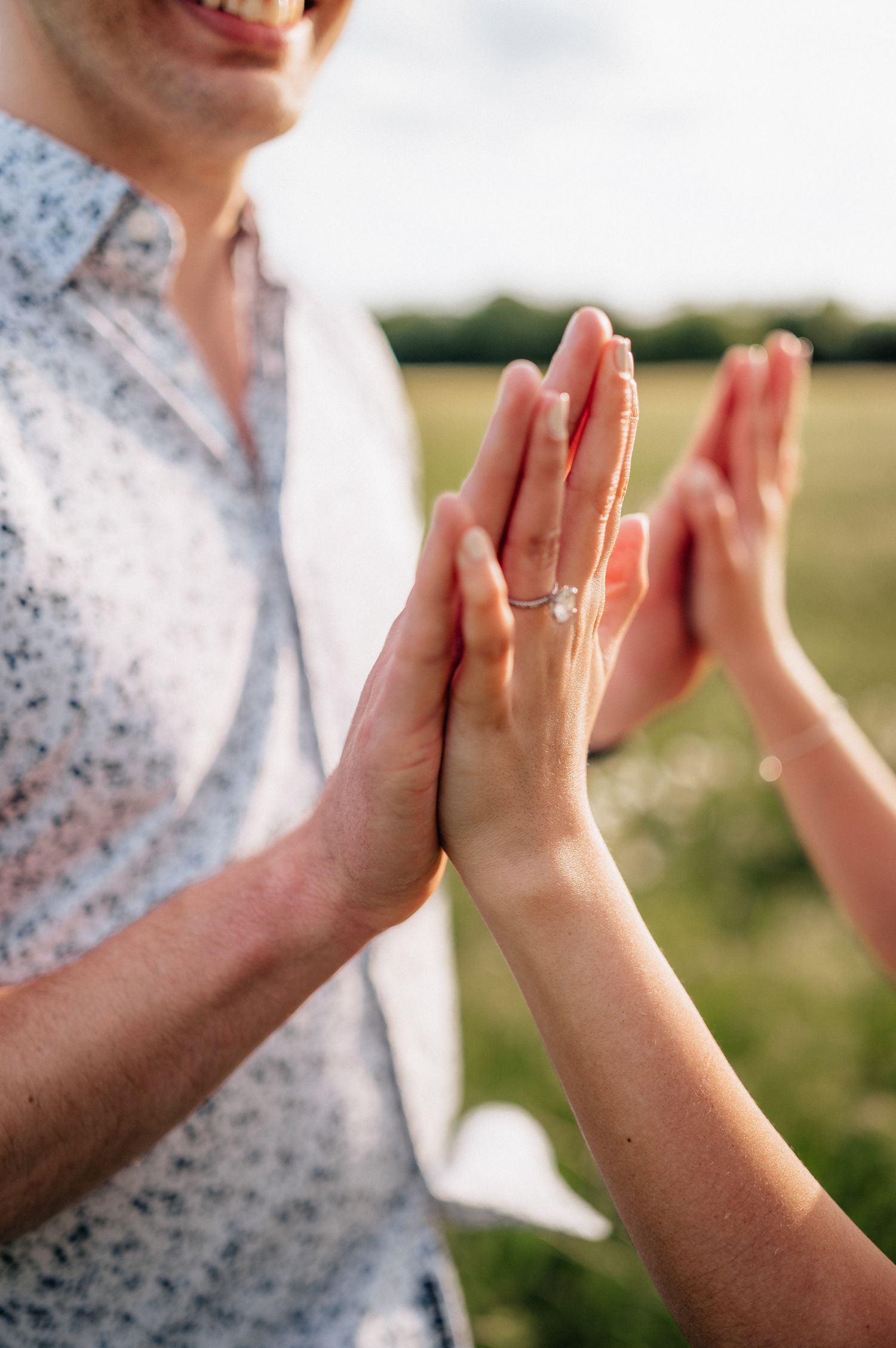Close-up of hands giving high-five with engagement ring visible in outdoor setting.