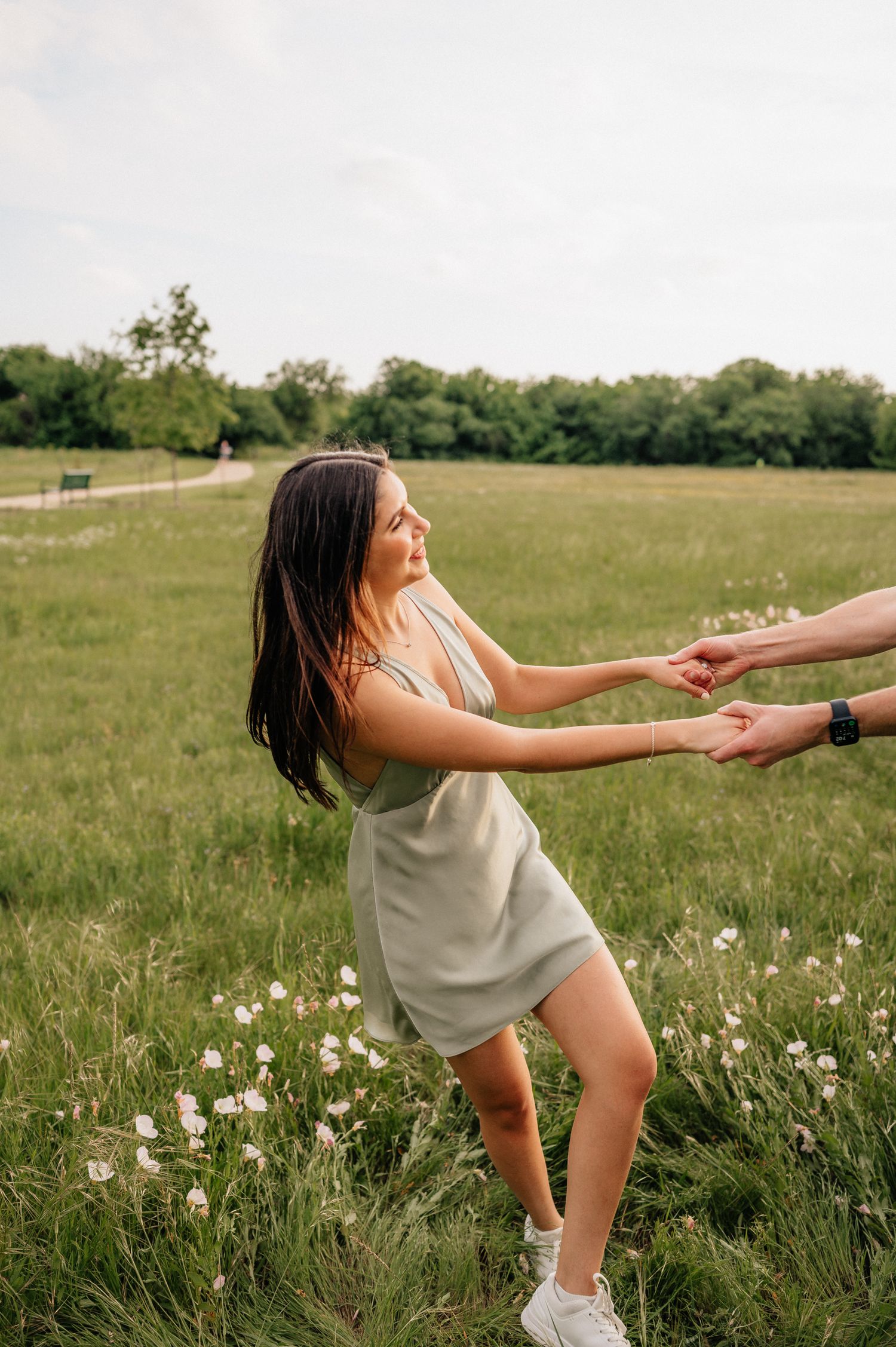 Person in light dress playfully leaning back while holding hands in a flowery meadow.