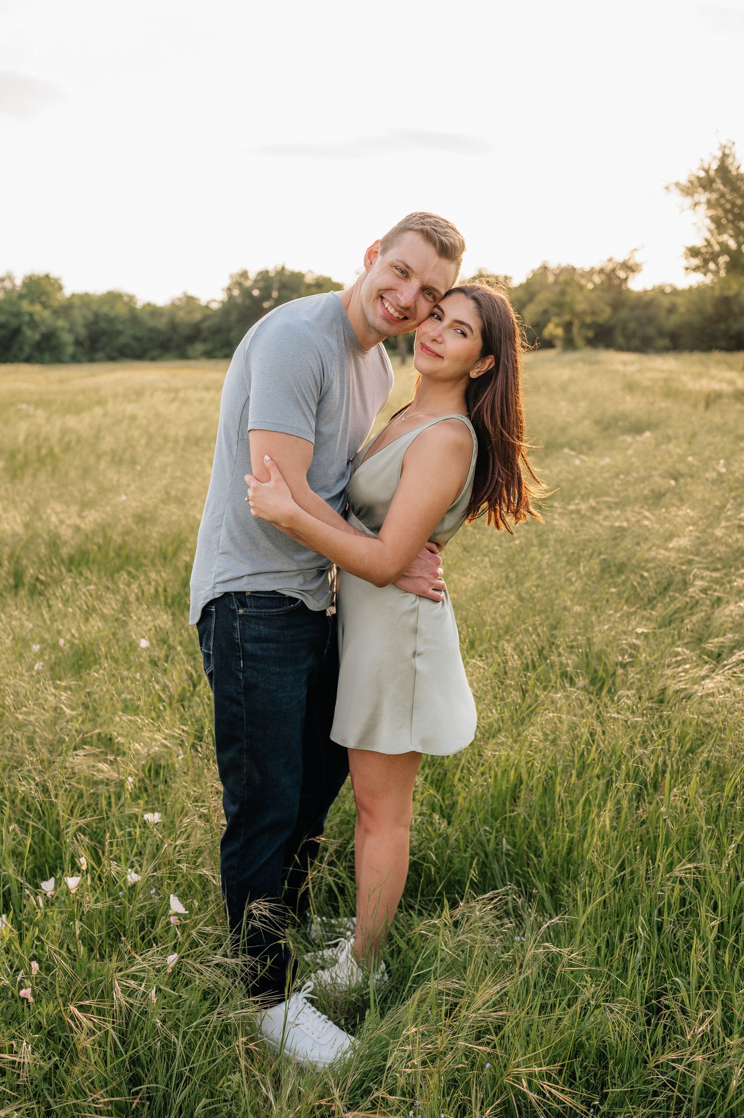 Happy couple sharing a loving embrace in a summer field with warm sunset lighting.