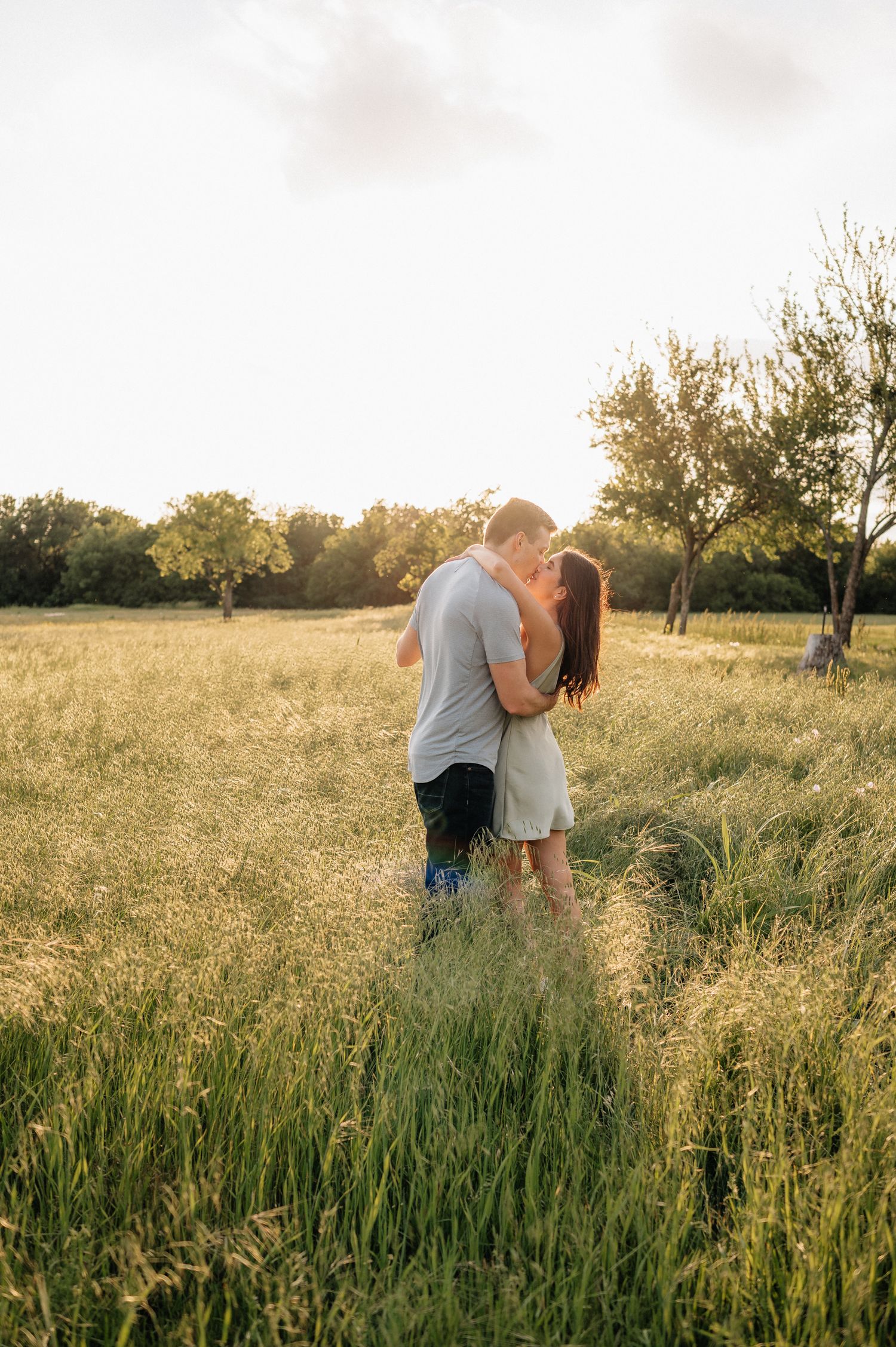 Intimate couple sharing a tender moment in a golden field at sunset surrounded by nature.