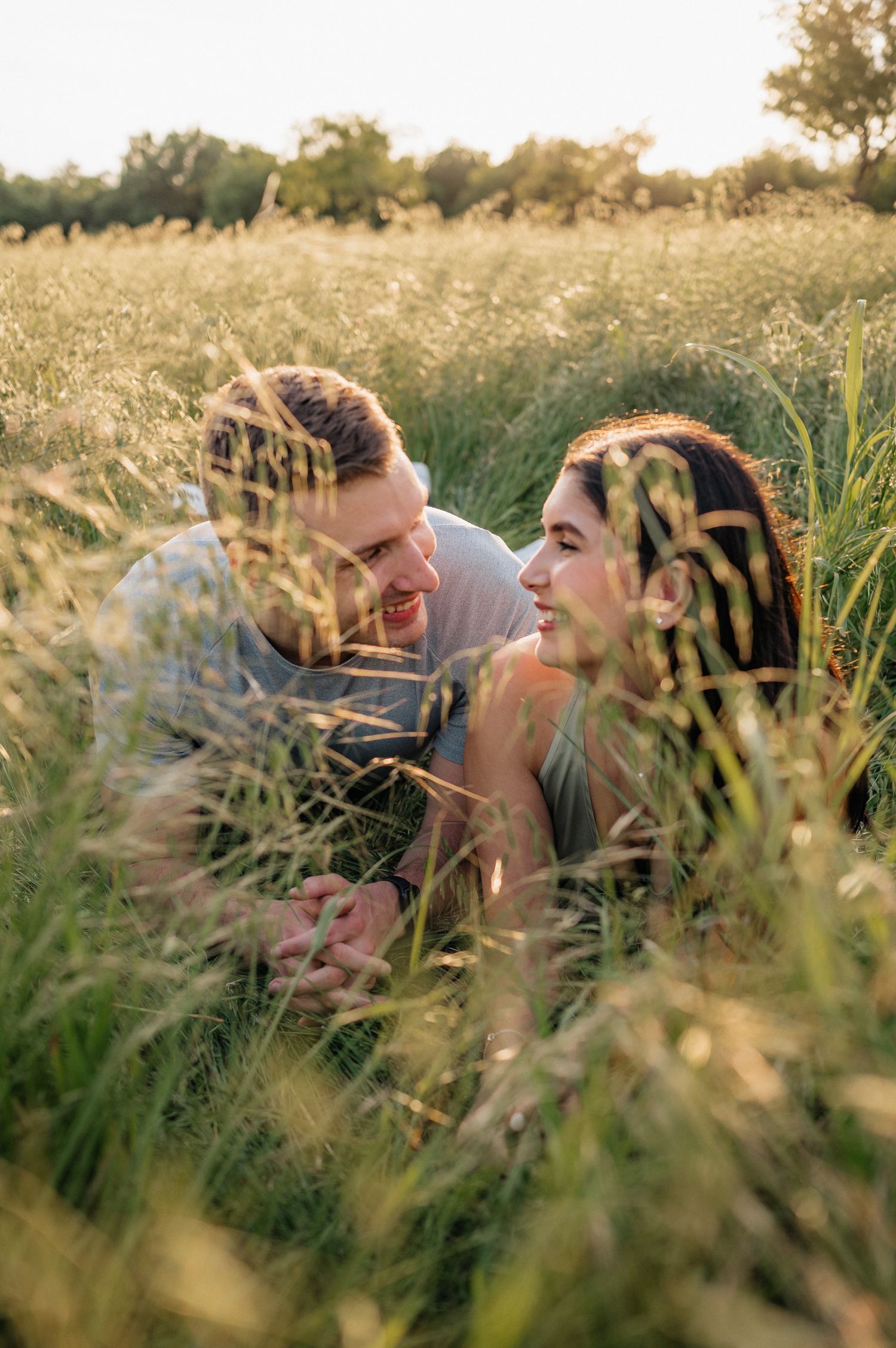 A couple laying in tall grass during golden hour surrounded by wildflowers.